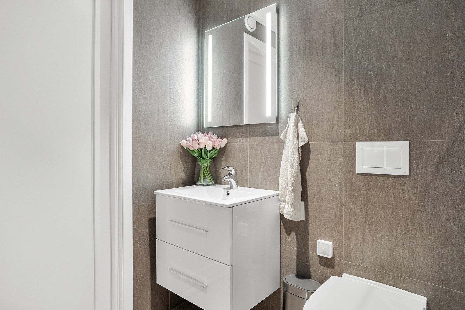 Store vegg- og gulvfliser er holdt i ulike gråtoner, og badet har downlights, varmekabler og vegghengt toalett. Galleribilde