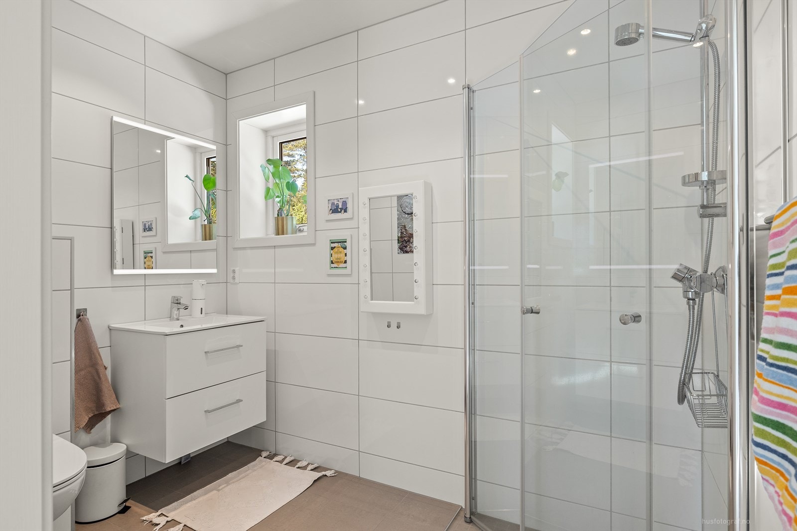 Badet har nedfelt servant, vegghengt toalett, dusj med svingbare dusjdører., skuffer i hvite glatte fronter og speil med justering av både styrke og fargetone . Galleribilde