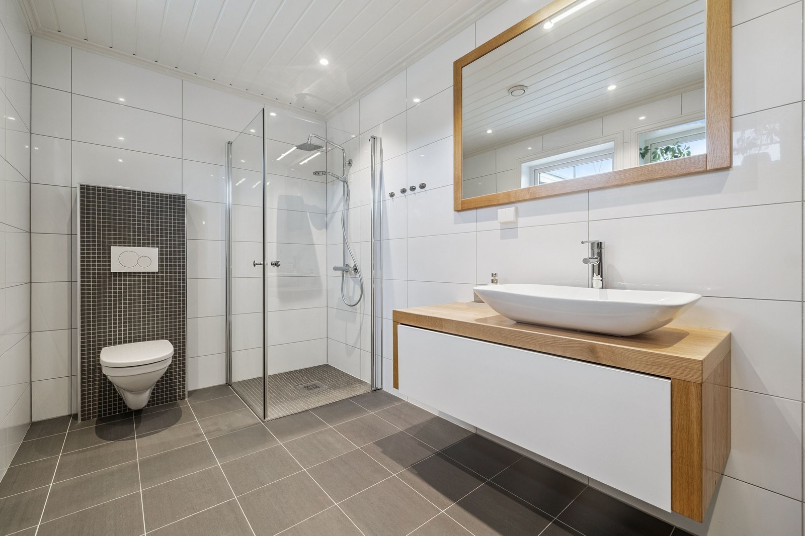 Badet i 1 etg er innredet med dusjhjørne med glassdører, vegghengt wc med innebygget sisterne, servantskap fra møbelsnekker med eikeomramning og
påliggende porselenssvask, speil med eikelister. Galleribilde