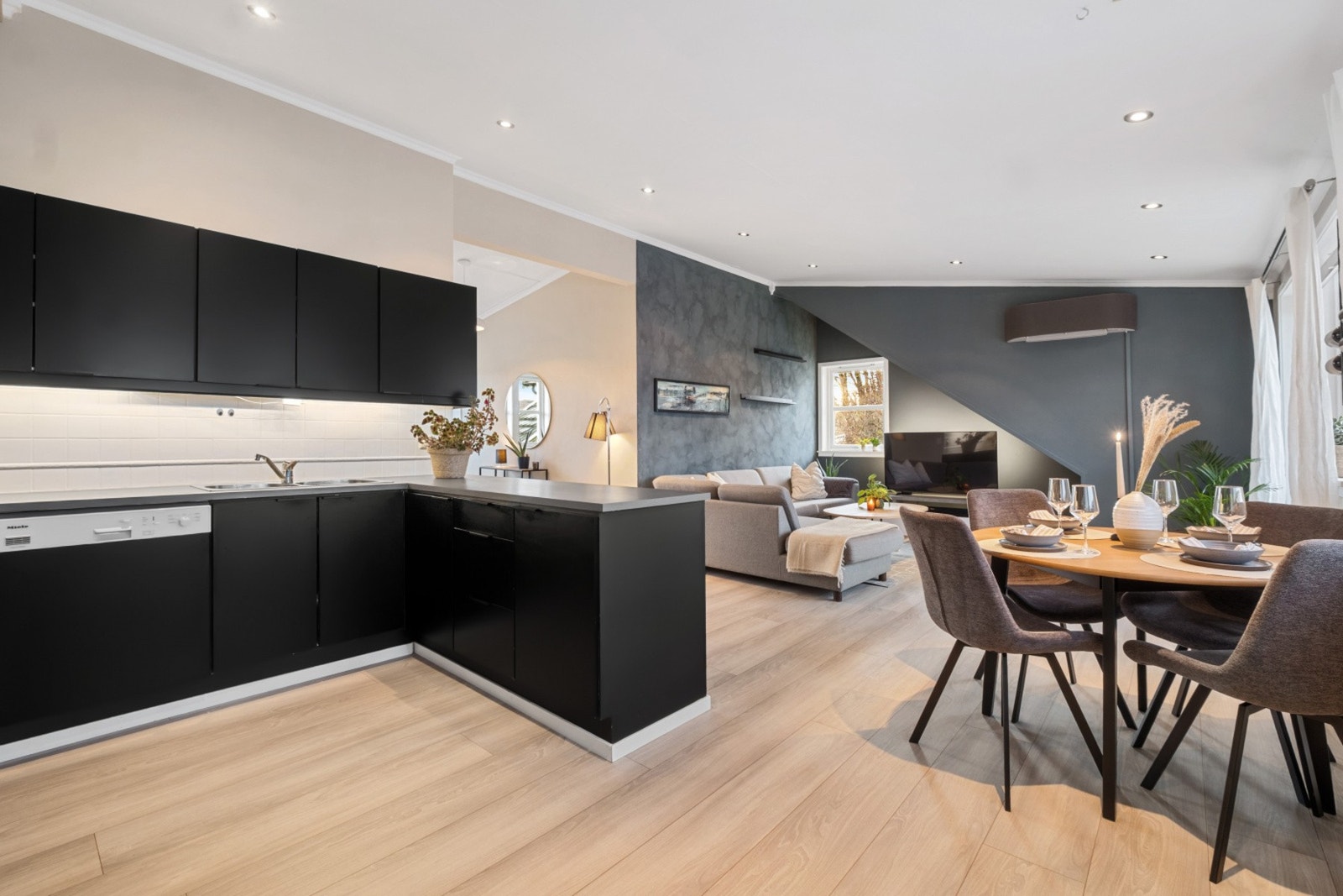 Nedfelt vask. Integrert platetopp, stekeovn og oppvaskmaskin. Fliser over benkeplate og lysarmatur under overskap. Galleribilde