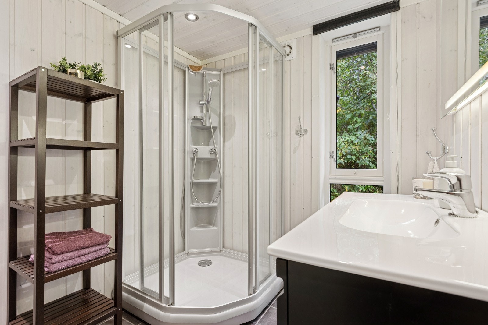 Badet er flislagt og utstyrt med dusjkabinett, klosett, servantskap og spil med lysdetaljer. Galleribilde