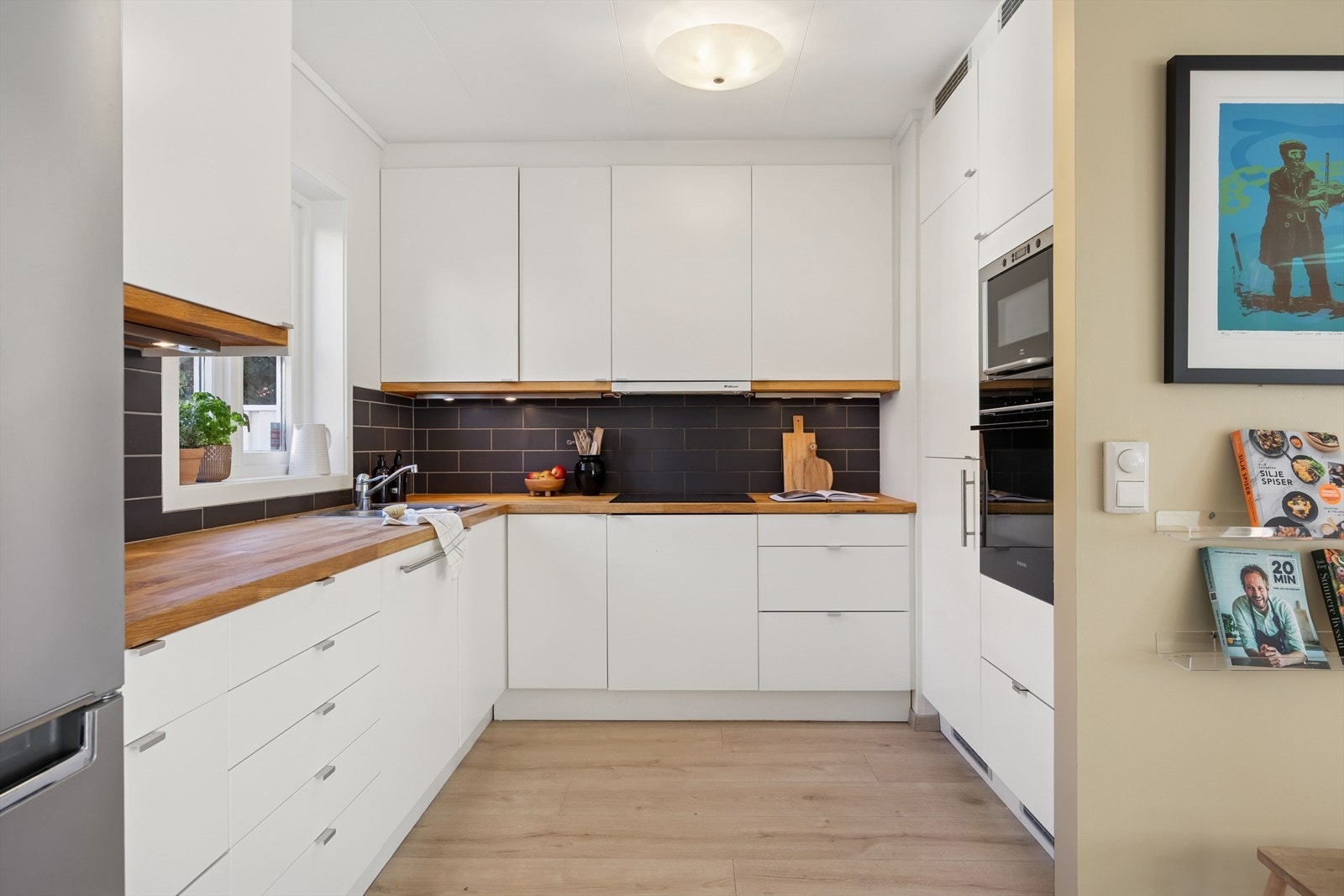 Kjøkken i åpen løsning fra stuen, med glatte fronter og heltre benkeplate. Utstyrt med komfyr, induksjonstopp, mikrobølgeovn, oppvaskmaskin og kjøl/frys. Galleribilde