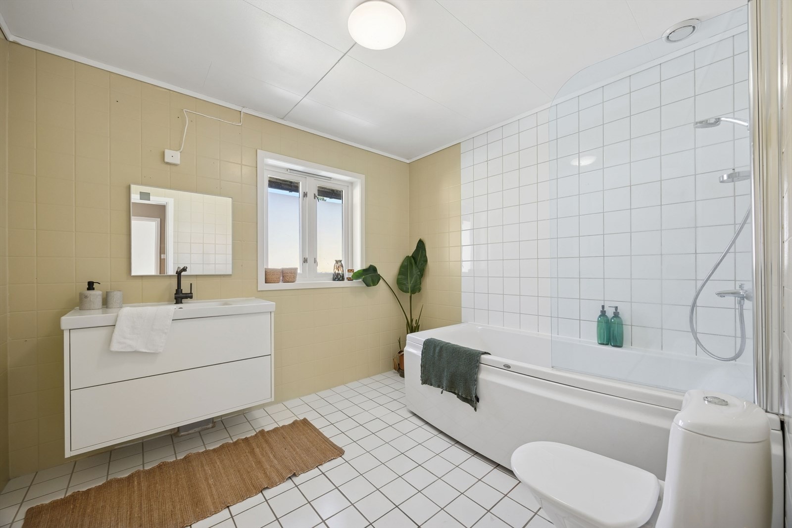 Lyst og flislagt bad i 2. etasje med elektriske varmekabler i gulv. Badet er utstyrt med badekar med dusjløsning, servantinnredning med speil og toalett. Galleribilde