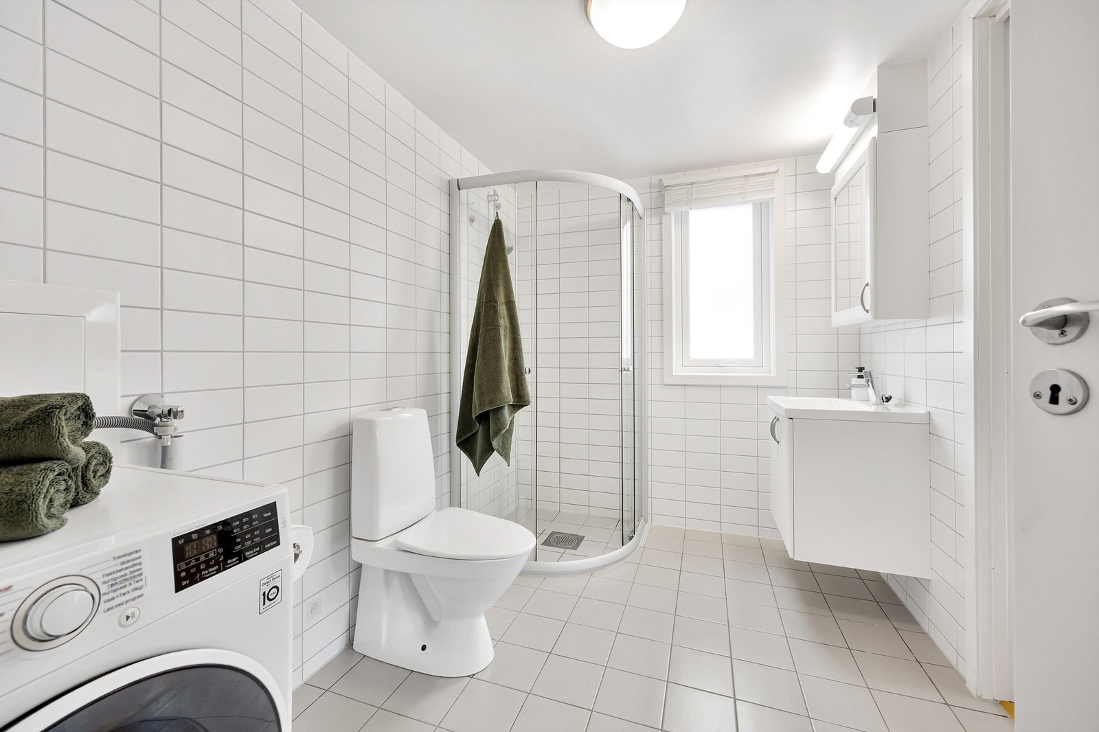 Badet er fra byggeår, med dusjkabinett og gulvstående toalett. Innredningen består av vegghengt skap med servant og overskap med speil og belysning over speilet. Galleribilde