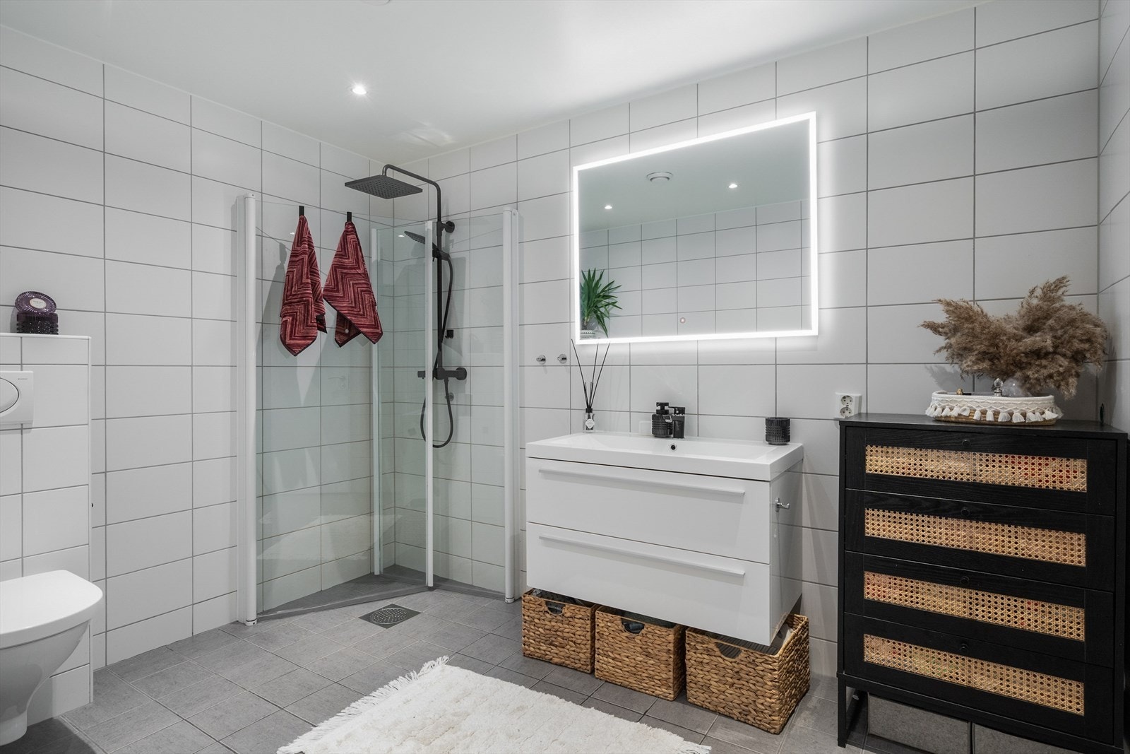 Lekkert flislagt bad med varmekabler i gulv, vegghengt toalett, svingbare dusjdører, servantskap og belyst speil. Galleribilde