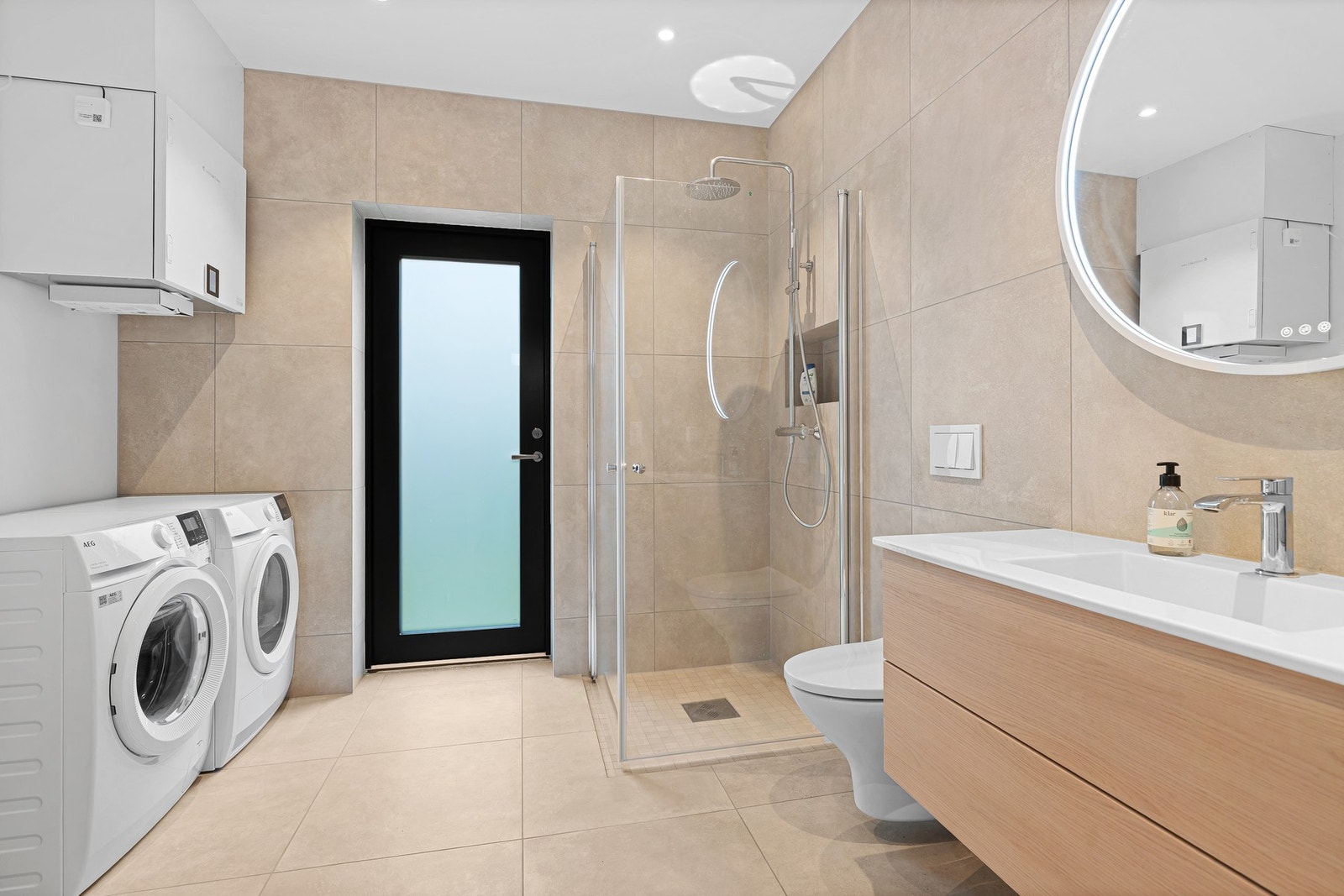 Badet er innredet med vegghengt toalett, servant med innredning, dusjhjørne og opplegg for vaskemaskin. Galleribilde