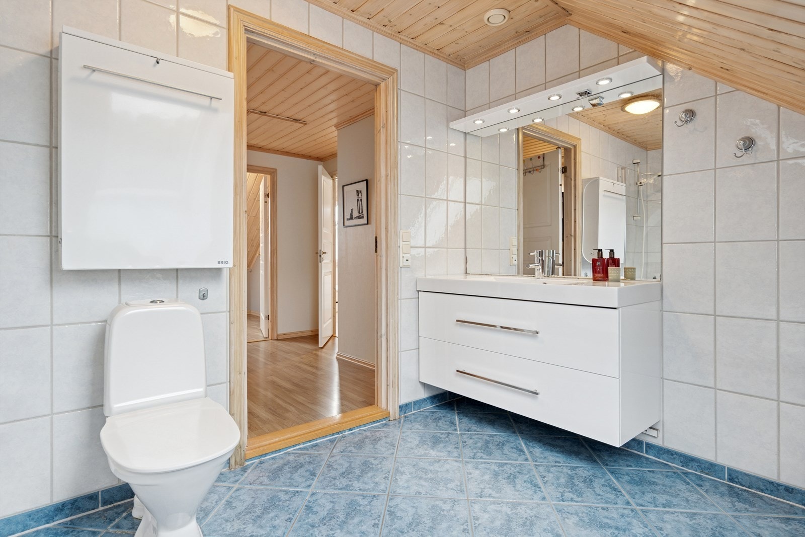 Innredning med nedfelt servant, toalett og badekar med dusjgarnityr på vegg og glassdør. Galleribilde