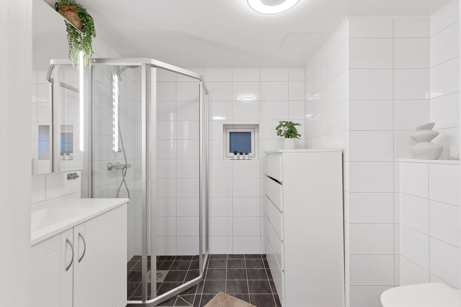 Videre er badet innredet med servantskap med speil og lys, vegghengt toalett og dusjhjørne. Galleribilde