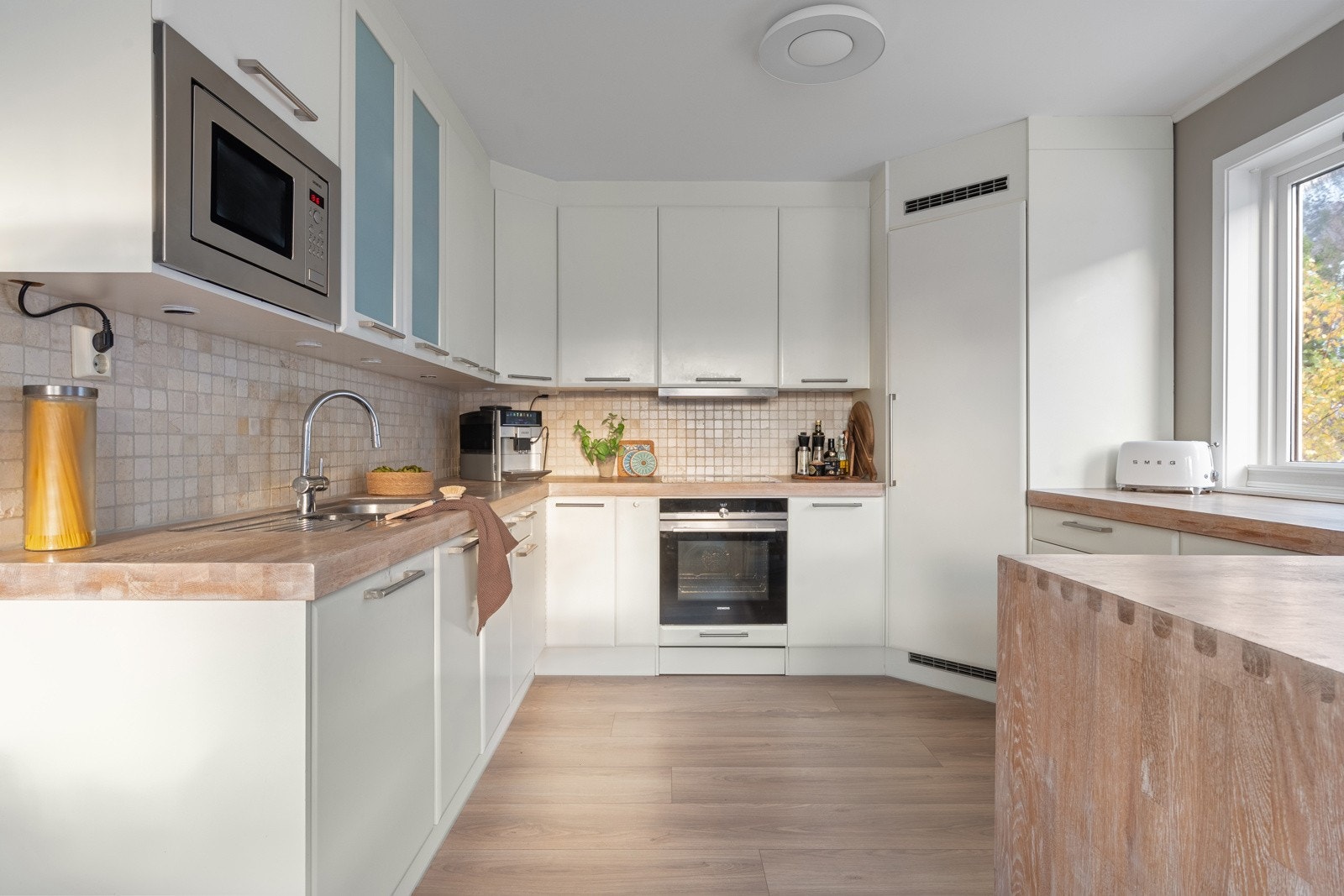 Pen kjøkkeninnredning med glatte fronter, heltre benkeplate med nedfelt oppvaskkum. Det er fliser over benk.