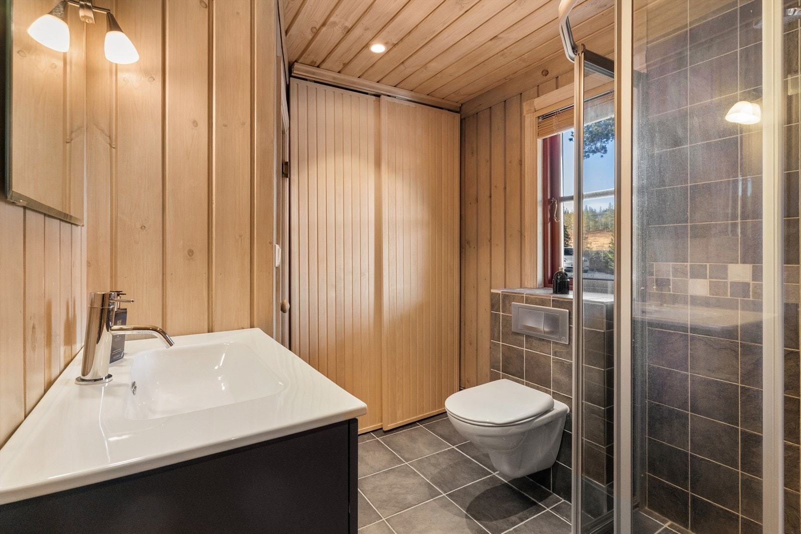 Badet er innredet med en lekker og eksklusiv servantløsning med plass til diverse oppbevaring og speil. Videre er badet utstyrt med toalett, dusjhjørne med innfellbare dusjvegger. Galleribilde