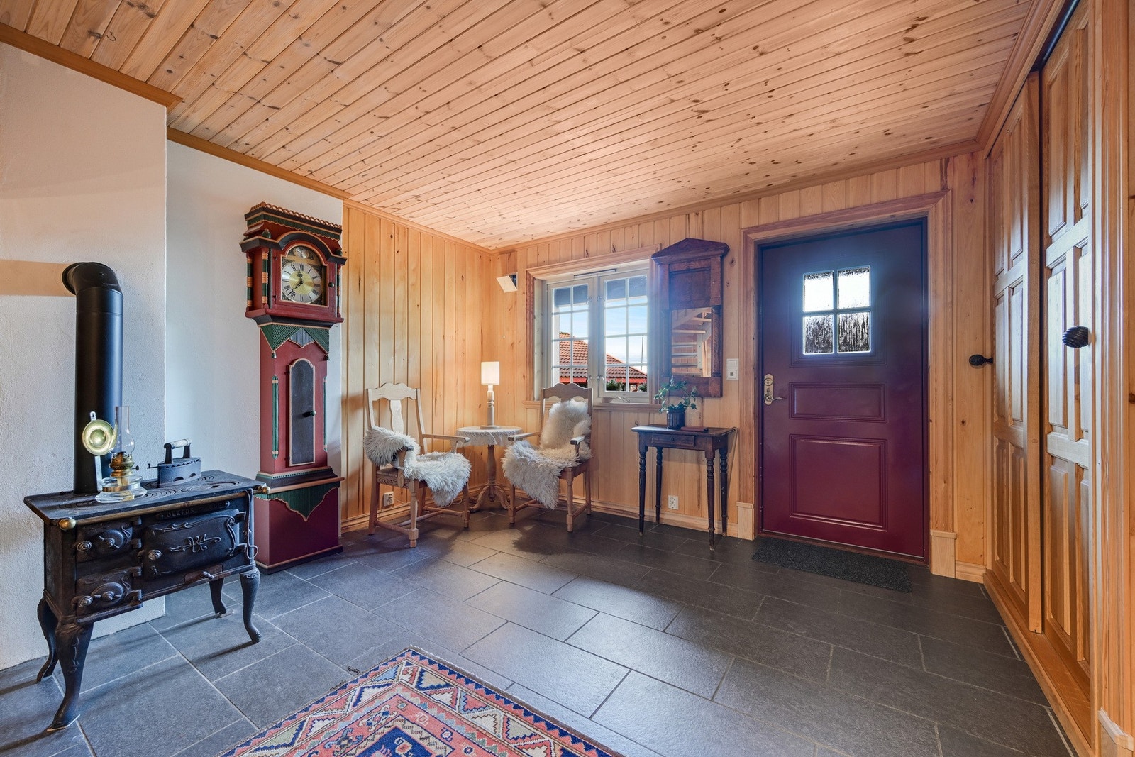 Hallen er flislagt og har elektriske varmekabler i gulvet. Veggene er kledd i flott lindepanel. Klær og sko kan oppbevares i den solide skyvedørsgarderoben med håndlagde dører i ask. Galleribilde