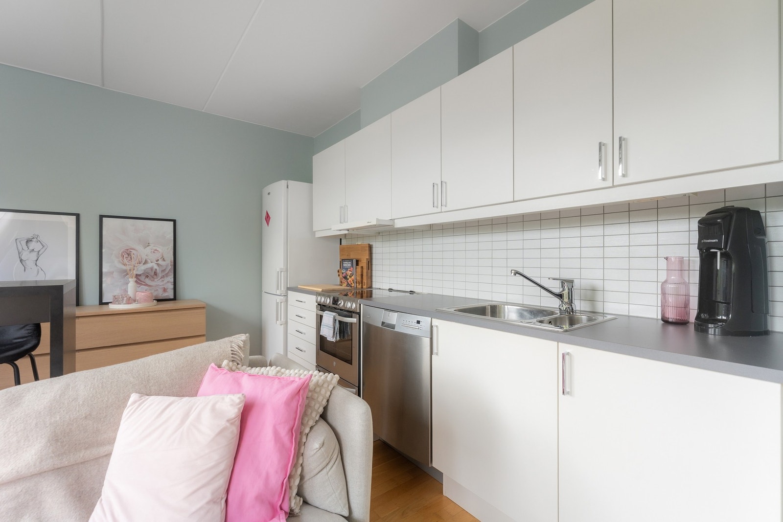 Moderne kjøkken fra Sigdal med hvite fronter, pen benkeplate i laminat, samt pene fliser over benk. Det er avsatt plass til kjøleskap/frys, komfyr og oppvaskmaskin. Galleribilde