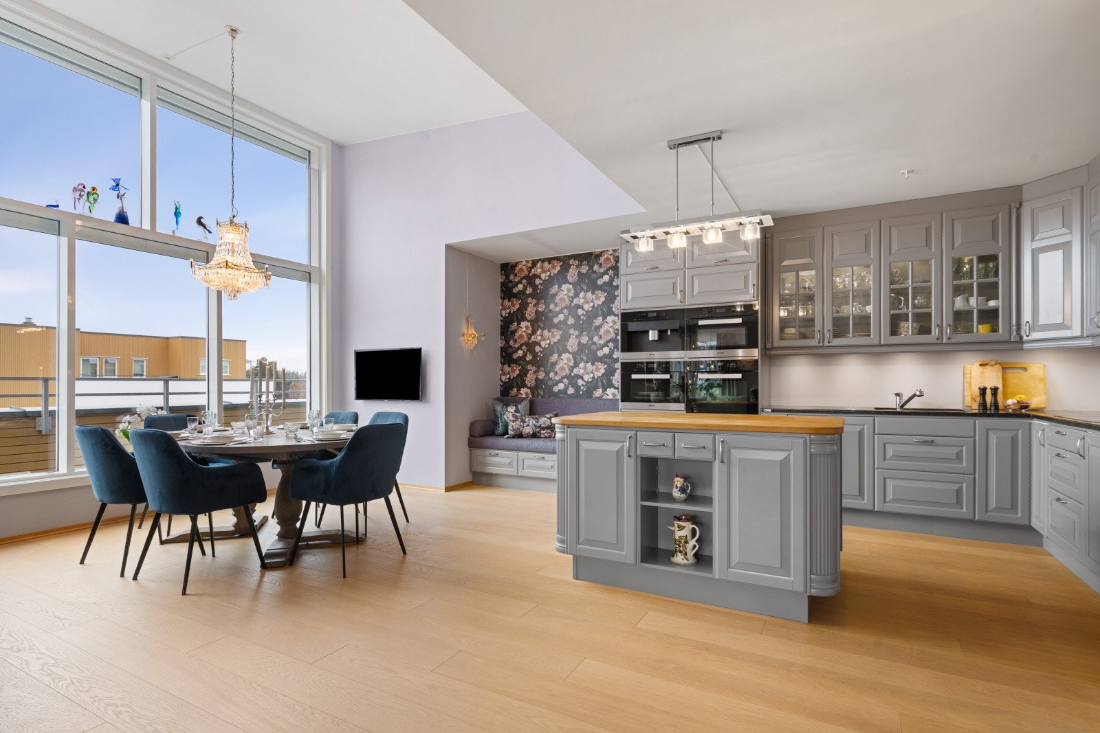 Påkostet kjøkkeninnredning med profilerte fronter og overskap med glass. Det er malte flater over steinbenk med komposittkum og ett-greps blandebatteri. Galleribilde