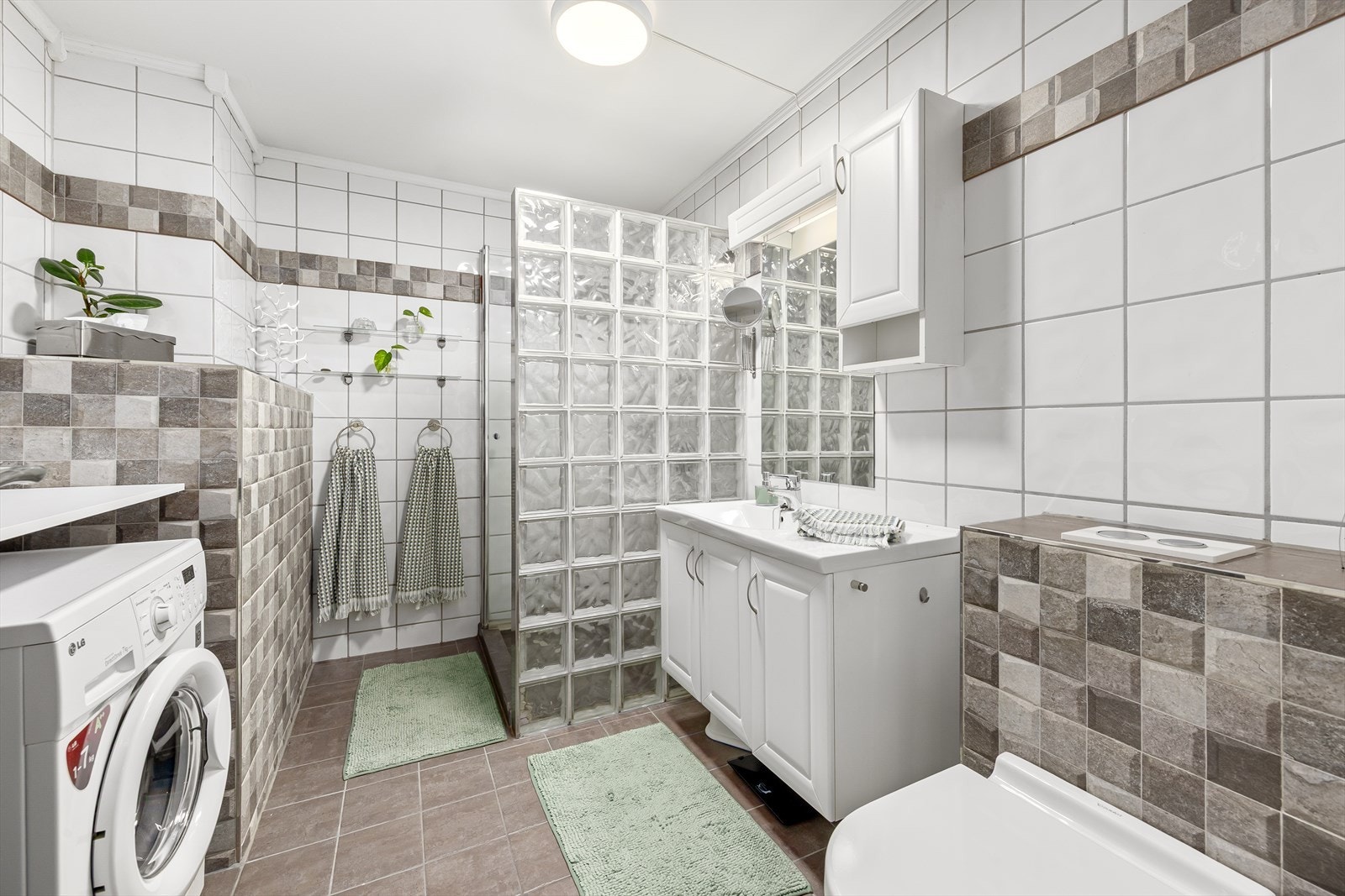 Delikat flislagt bad med behagelige varmekabler i gulv. Badet er utstyrt med dusjhjørne, vegghengt toalett, opplegg for vaskemaskin og lys baderomsinnredning. Galleribilde