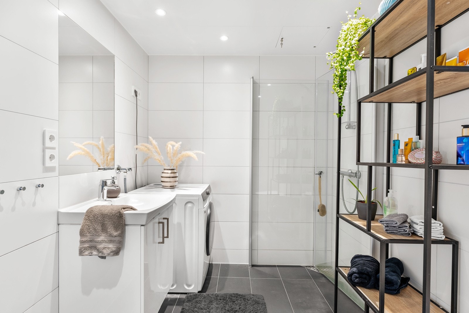 Baderommet har lyse, lettstelte vegger og kontrasterende mørke gulvfliser. I tillegg har rommet smarte innfellbare dusjdører, opplegg for vaskemaskin og spotbelysning i tak. Galleribilde