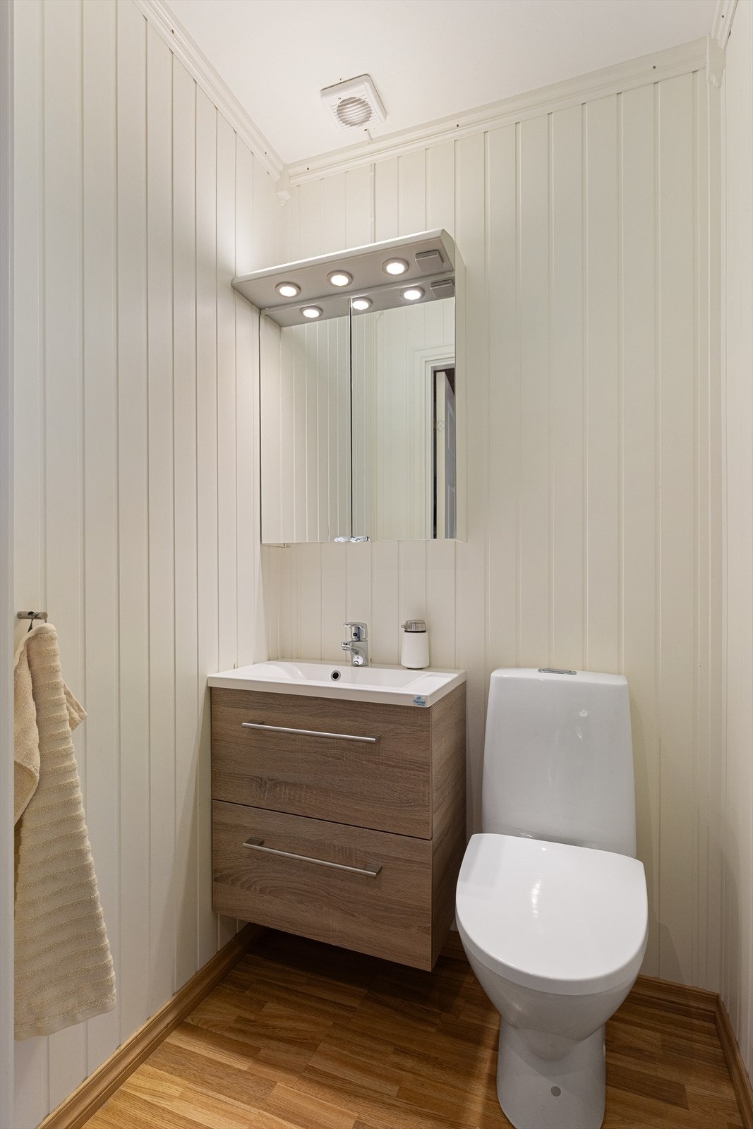 Separat WC med gulvstående klosett og servant med underskap. Det er integrert belysning over speilskap. Galleribilde