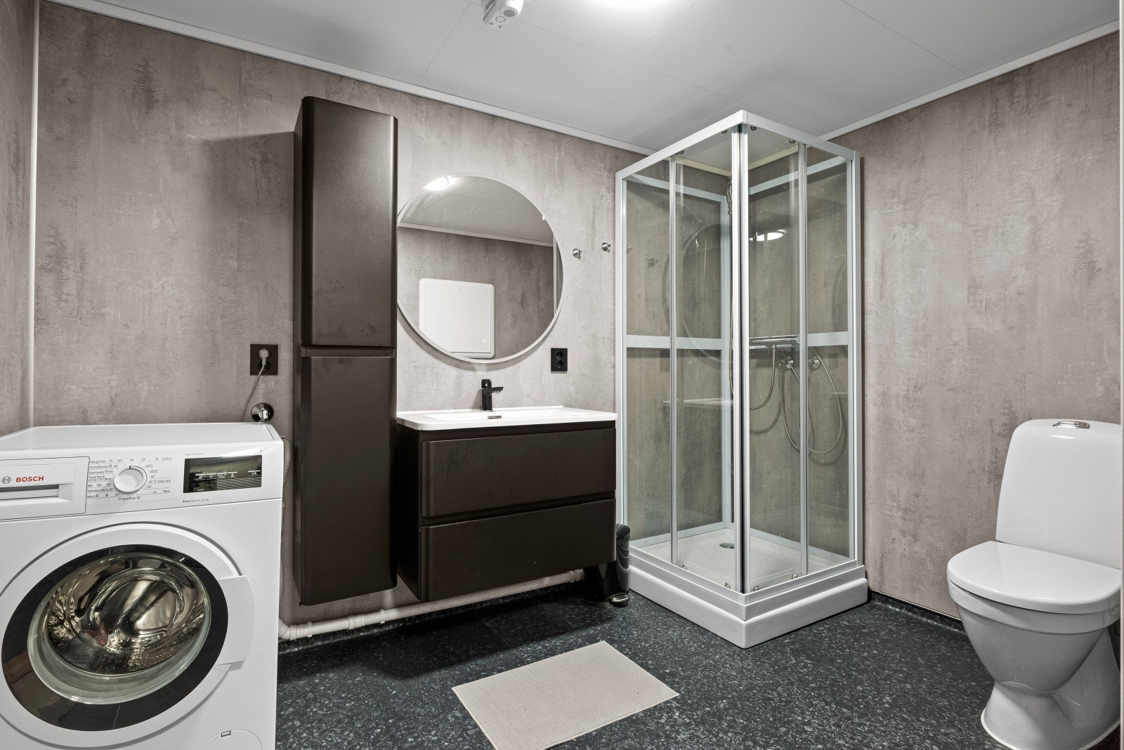 Den mørke innredningen har glatte fronter, matchende høyskap, heldekkende servant og stort, rundt speil Galleribilde