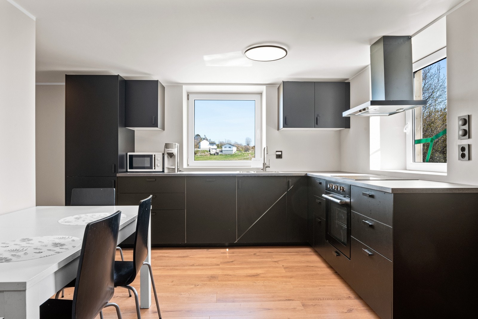 Kjøkkeninnredningen er stilren med sorte, glatte fronter, lys benkeplate, integrerte hvitevarer og ventilator Galleribilde