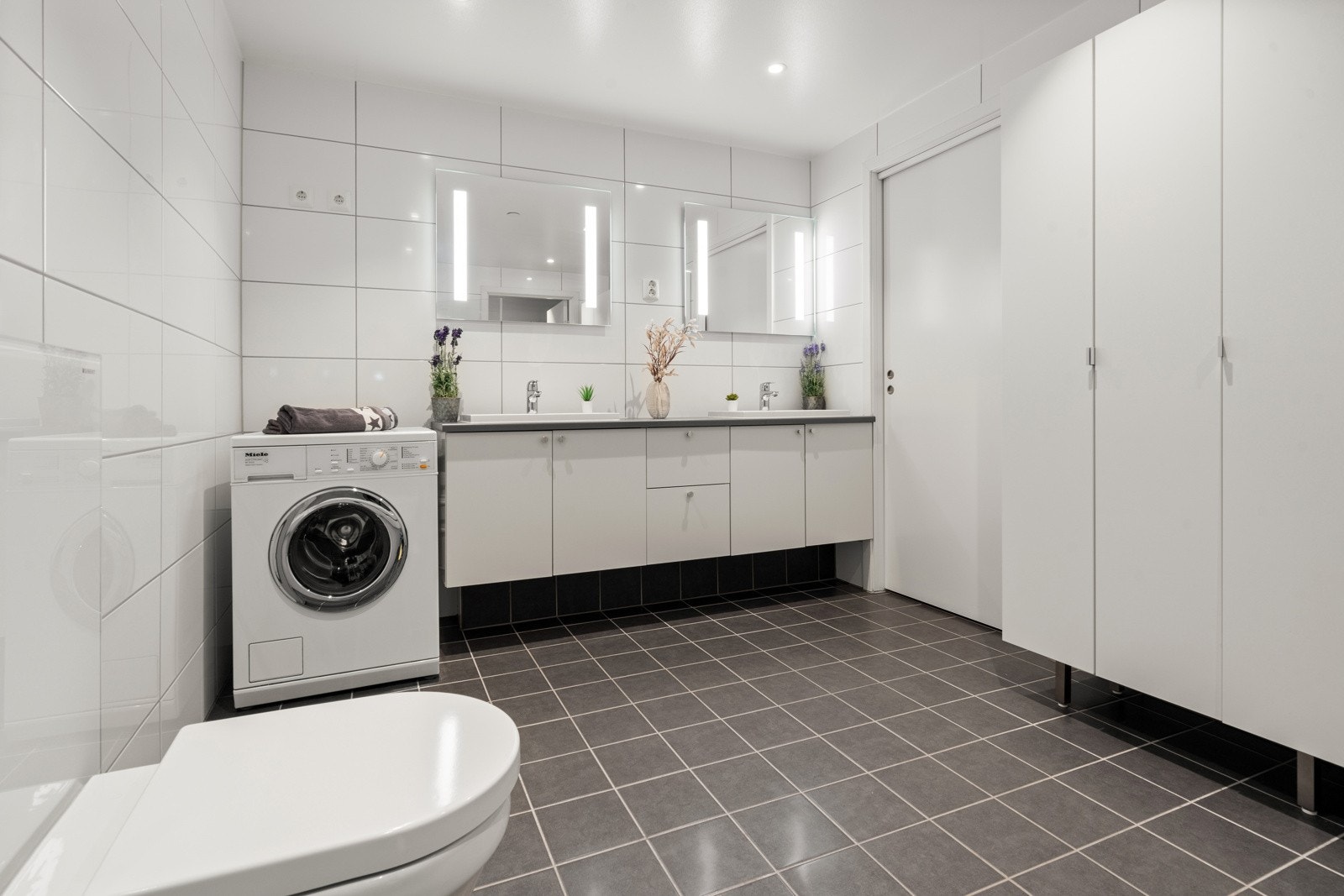 Videre har badet vegghengt toalett, dusjhjørne med glassdører og opplegg for både vaskemaskin og tørketrommel. Galleribilde