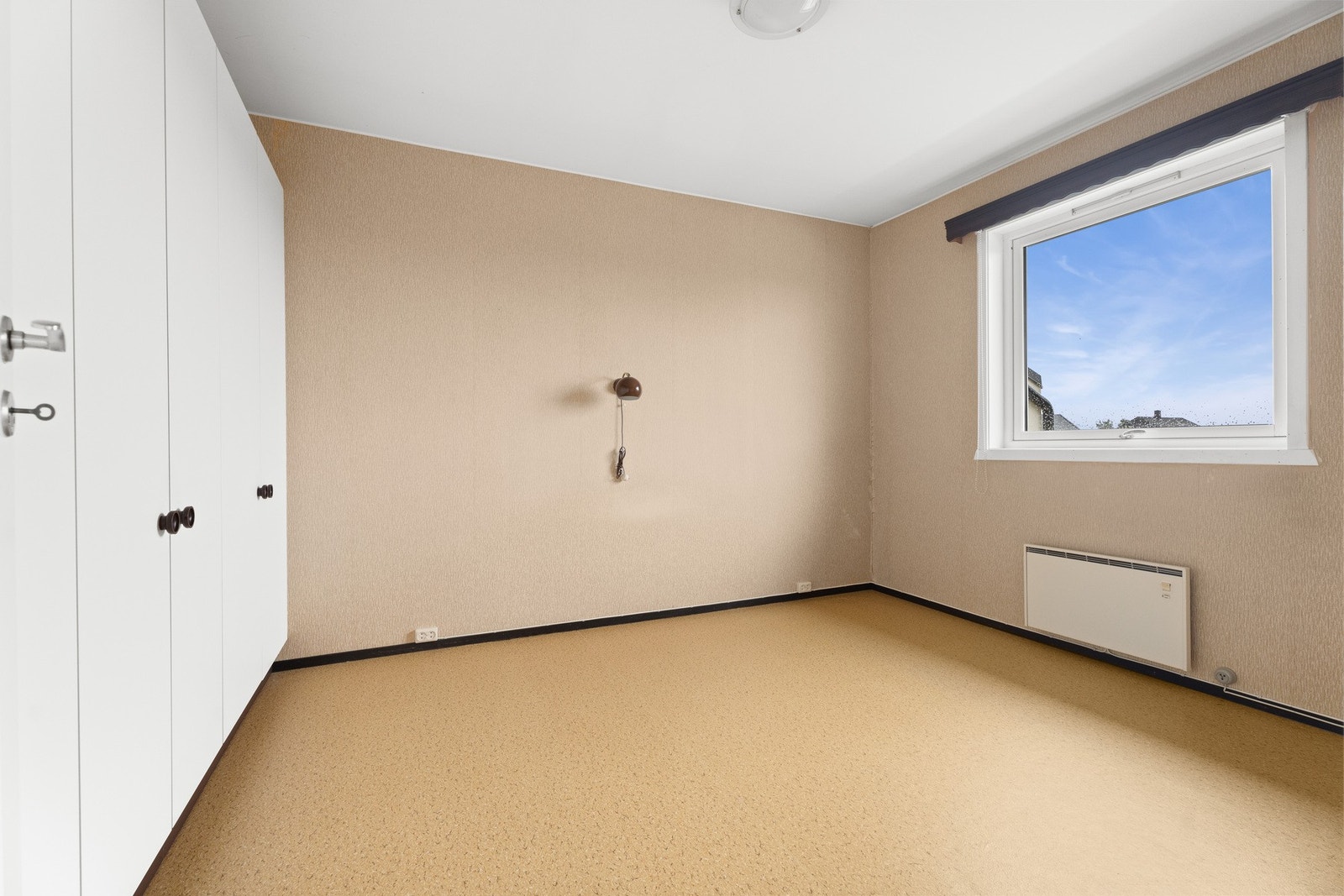 Leiligheten har et luftig og romslig soverom med beige tapet på veggene og matchende belegg på gulvet Galleribilde