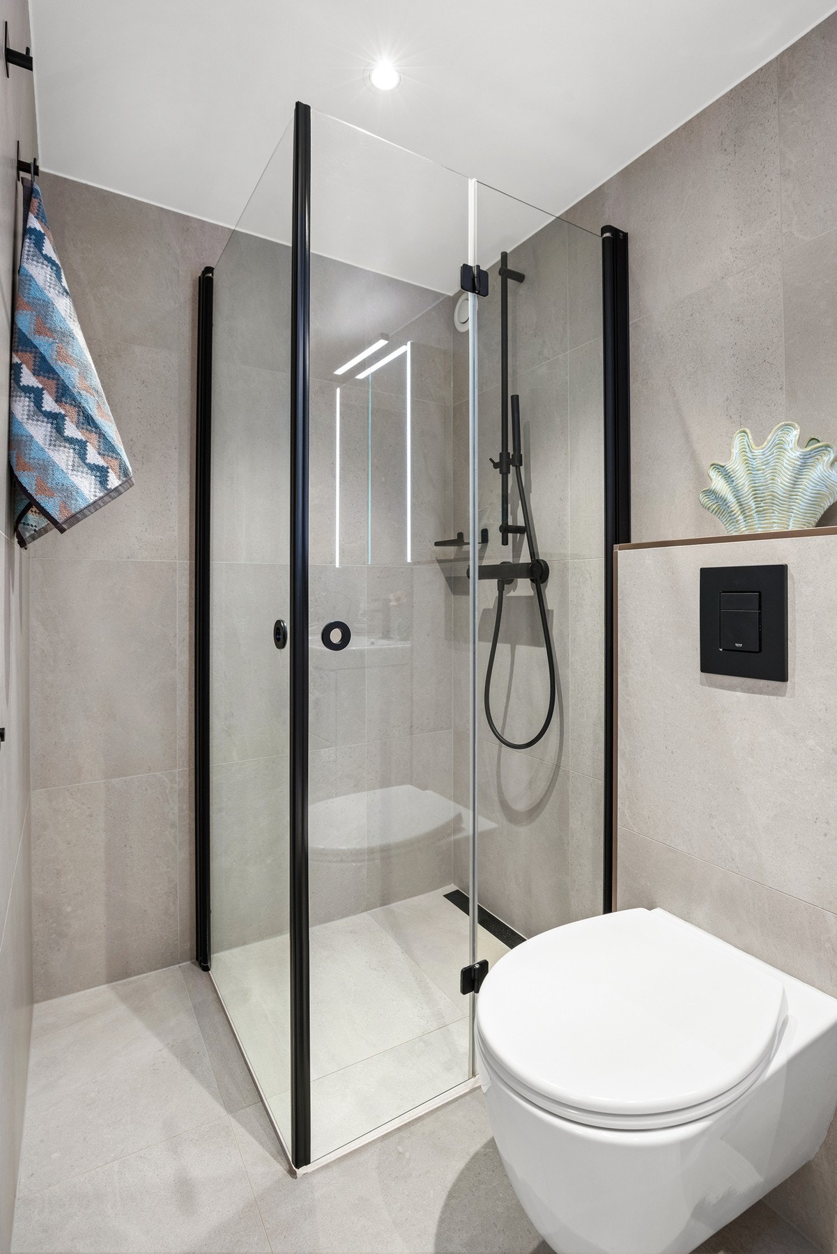 Badet har flotte, store fliser i en delikat farge, og sorte detaljer som setter et stilig preg på baderommet Galleribilde