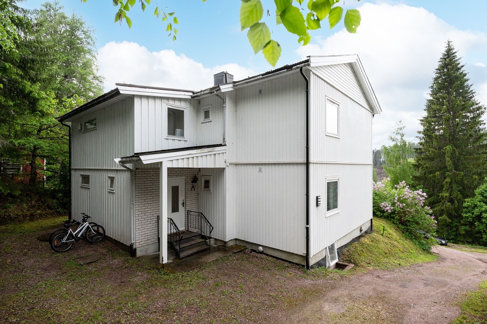 Tomten har gruset innkjøring og gårdsplass, samt hage i front med prydbusker, ellers trær og prydbusker som rammer tunet fint inn. Overbygd inngangsparti skjermer for vær og vind. Galleribilde