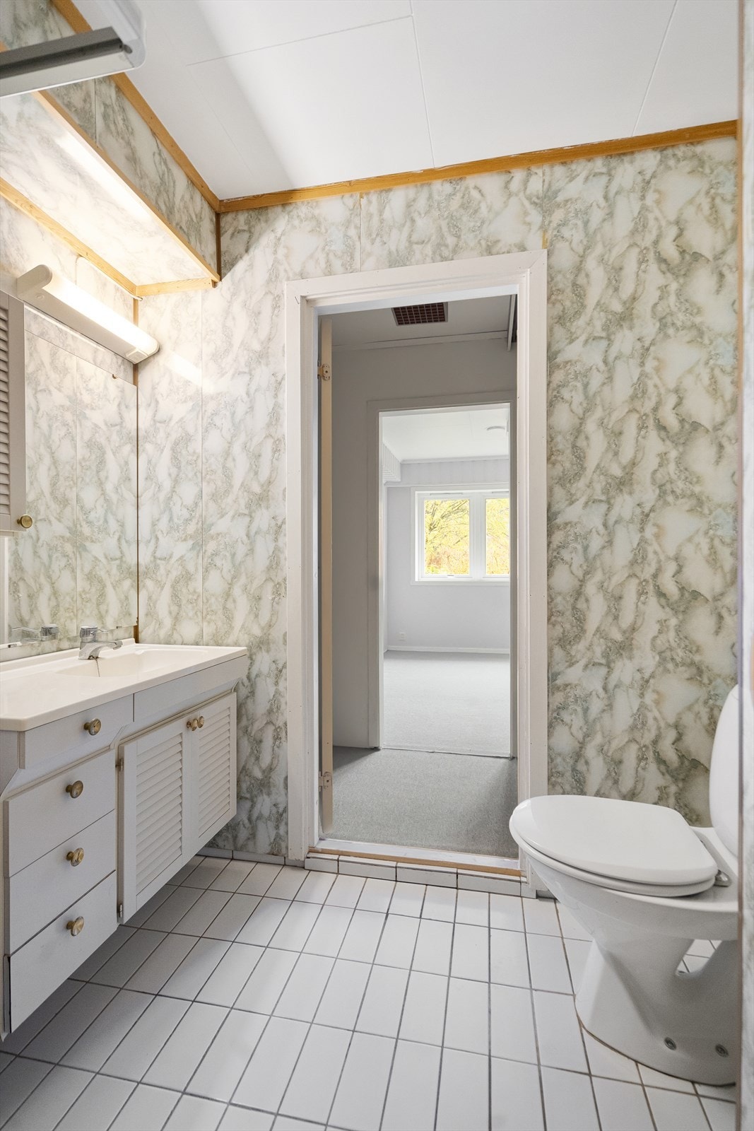 Badet er utstyrt med flislagt gulv, servant, speilskap og toalett Galleribilde