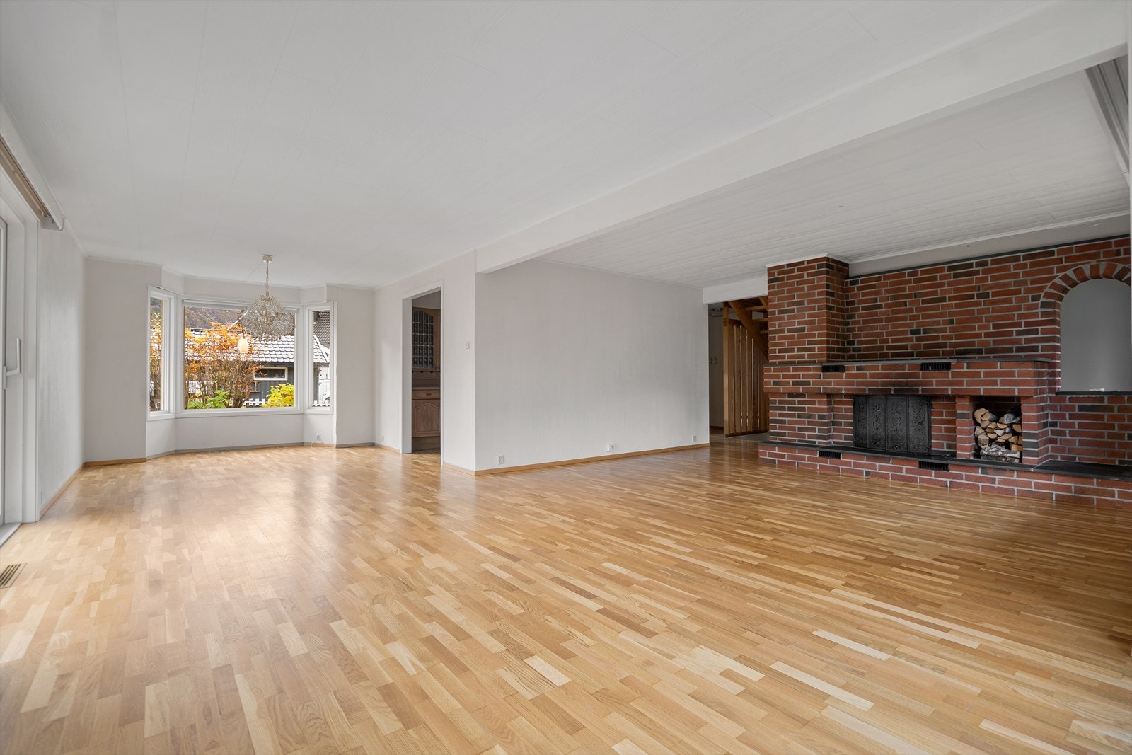 Stor og innbydende stue med store vinduer, god takhøyde og klassisk teglsteinpeis som gir både sjarm og varme til stuen Galleribilde