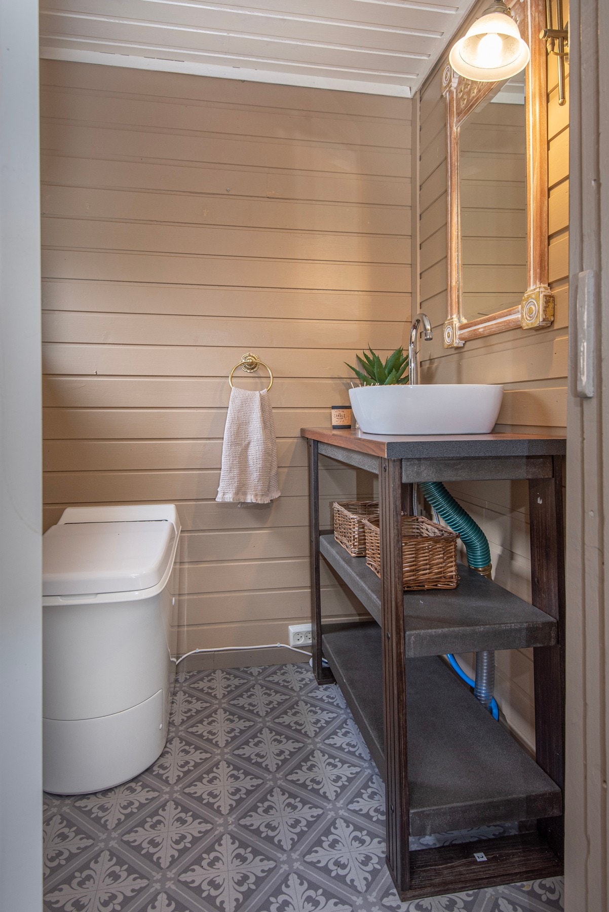 Toalettrom med Cinderella forbrenningstoalett. På gulvet er det vinyl og malte panelte vegger. Galleribilde