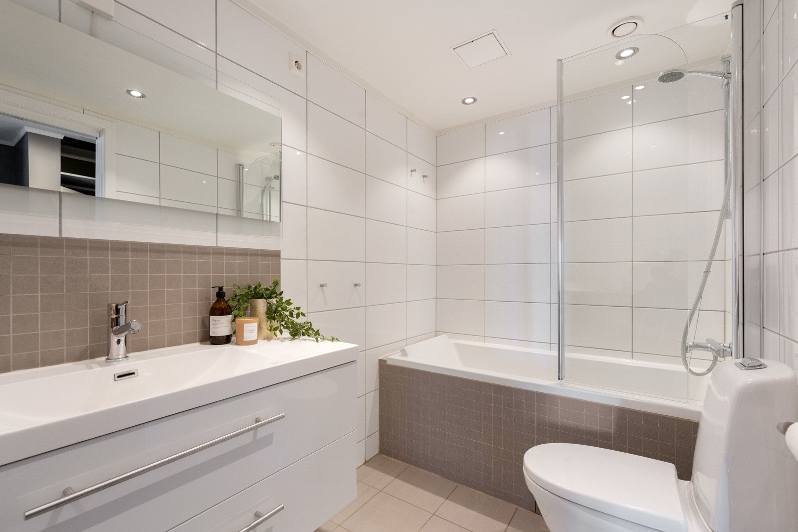 Badet er utstyrt med servant i innredning med speil og belysning over, badekar med dusjgarnityr, toalett og plass/opplegg for vaskemaskin Galleribilde