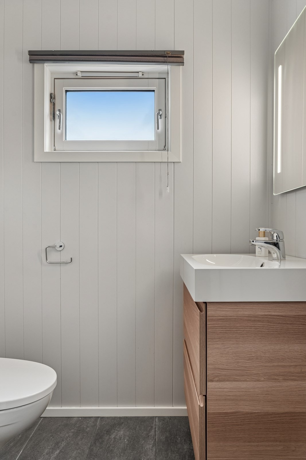 Toalettrom har malt plate på vegg og fliser på gulv. Innredet med toalett og håndvask. Plissègardin. Ventilasjon er utført med ventil i vindu. Galleribilde