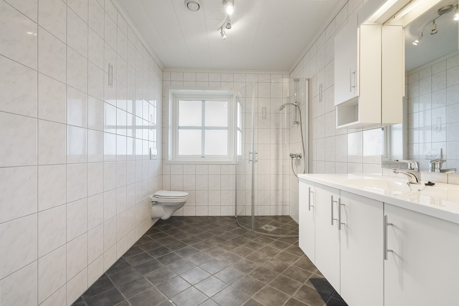 Heilflisa bad også i underetasjen med vegghengt klosett, dusjhjørne og baderomsinnredning med over- og underskap Galleribilde