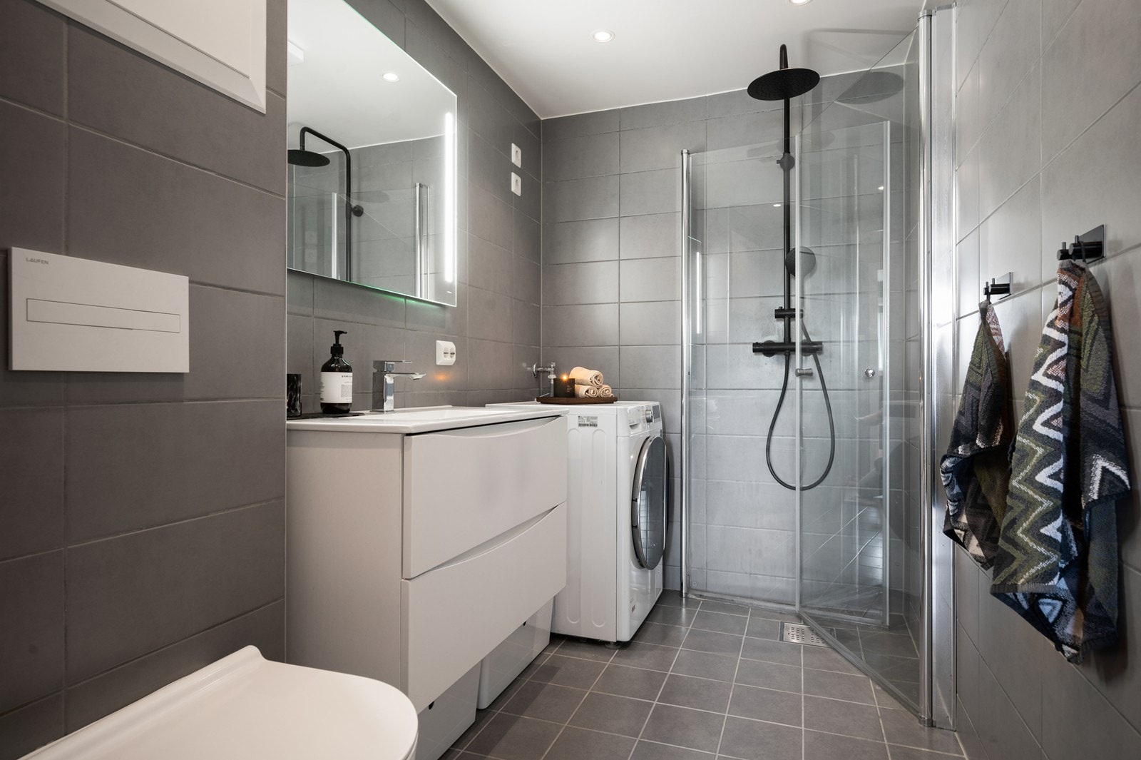 Videre er badet utstyrt med opplegg for vaskemaskin og dusjhjørne med innfellbare dører for plassbesparelse Galleribilde
