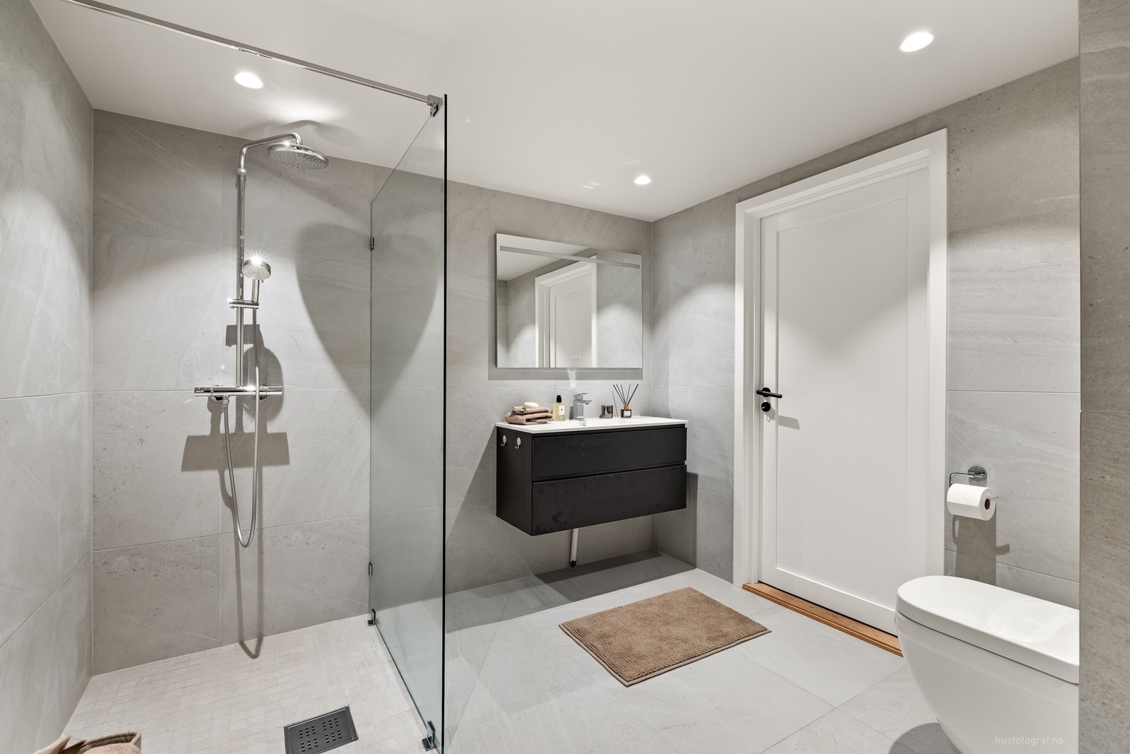 Speil med integrert belysning. Dusjhjørnet har glassvegg, og toalettet er vegghengt for et moderne og stilrent uttrykk Galleribilde