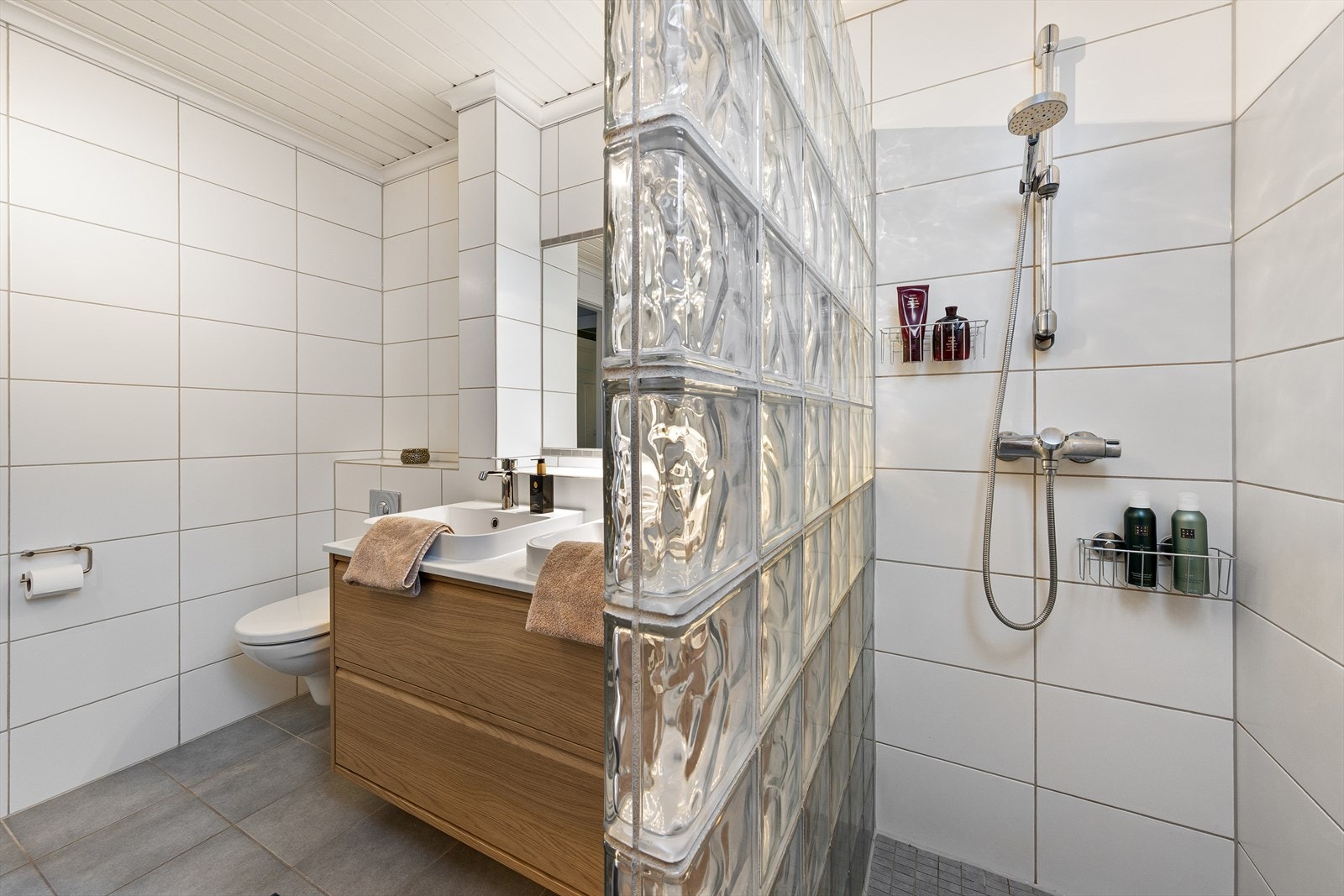 Badet er utstyrt med dusjhjørne, vegghengt toalett og en moderne baderomsinnredning med dobbelservant. Galleribilde