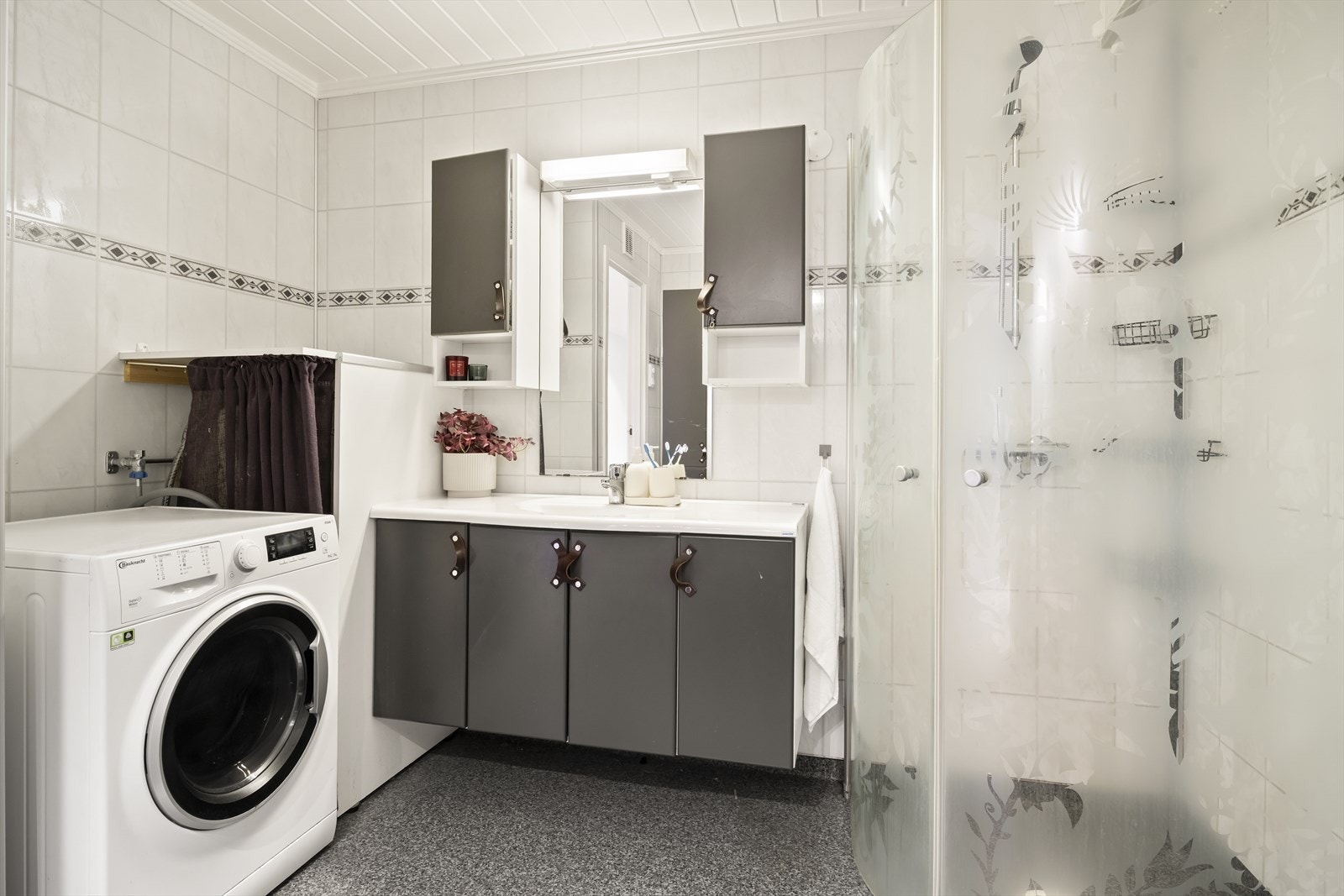 Badet er innredet med dusjhjørne med glassvegger og naturlig avtrekk - rikelig med baderomsinnredning og opplegg til vaskemaskin - komfort og kvalitet i ett Galleribilde