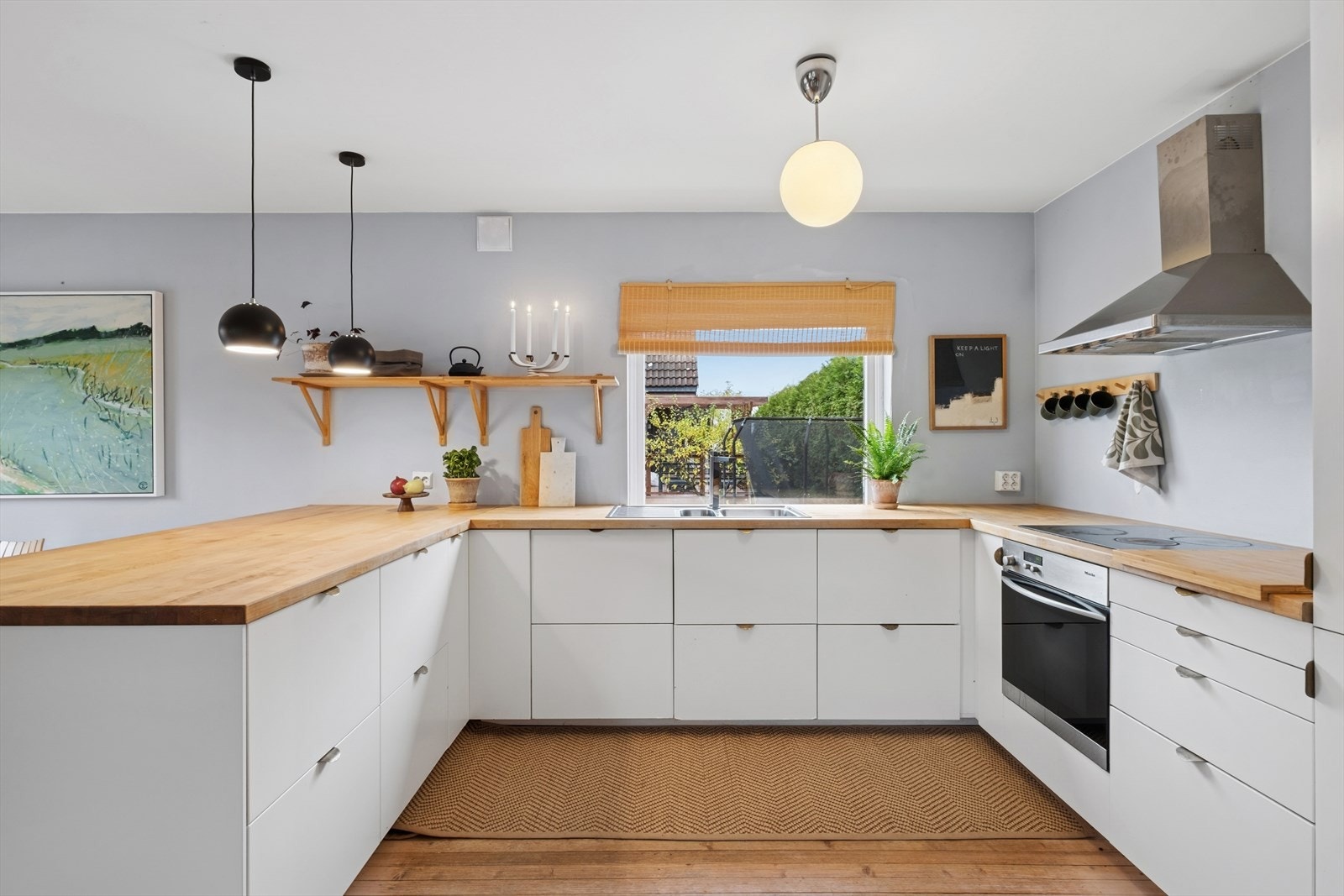 Lyst og funksjonelt kjøkken med hvite slette fronter, heltre benkeplate og oppvaskkum. Galleribilde