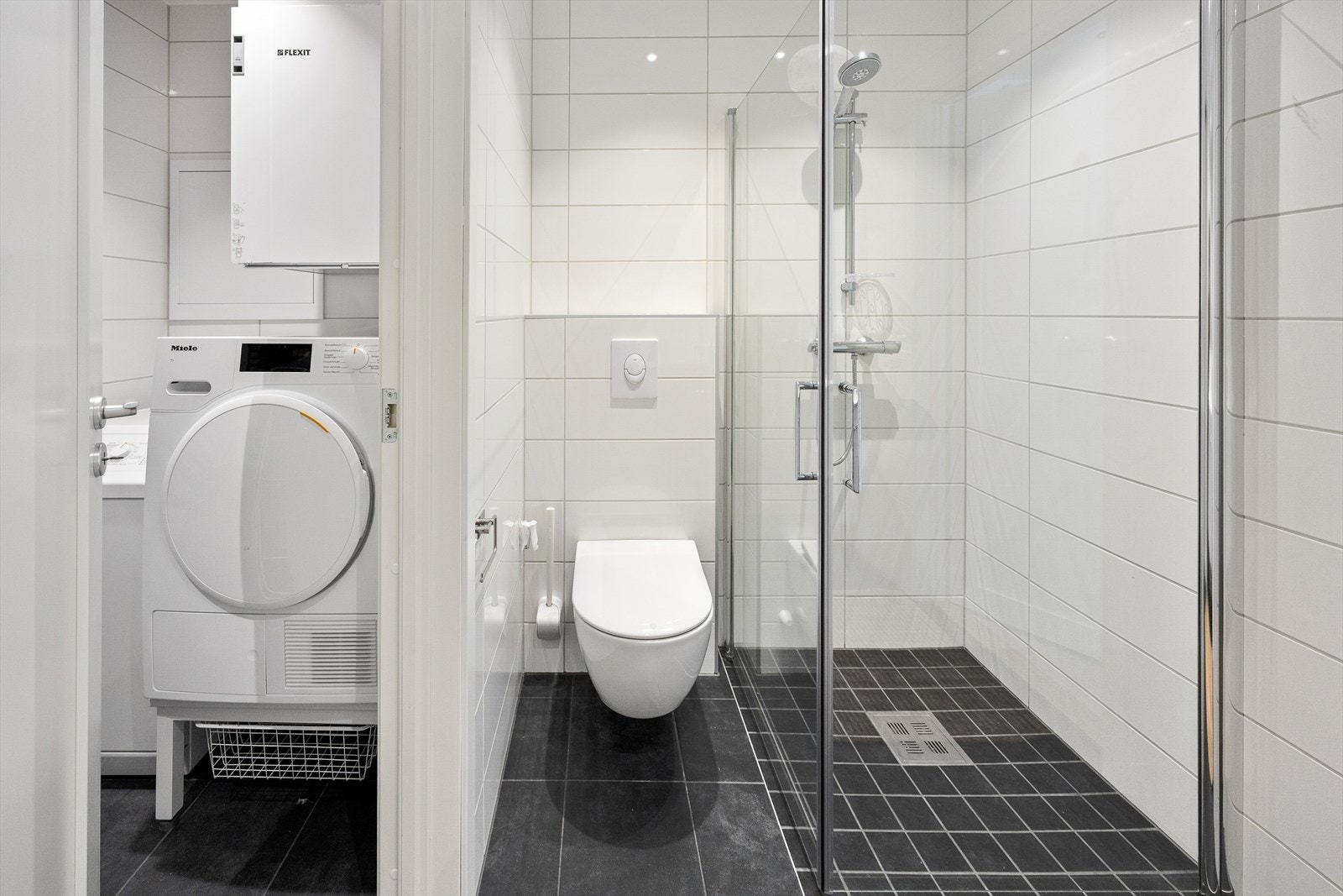 Dette badet fungerer som et kombinert gjestebad og vaskerom/teknisk rom - med blant annet opplegg for vaskemaskin, sentralstøvsuger og ventilasjonsanlegg. Galleribilde