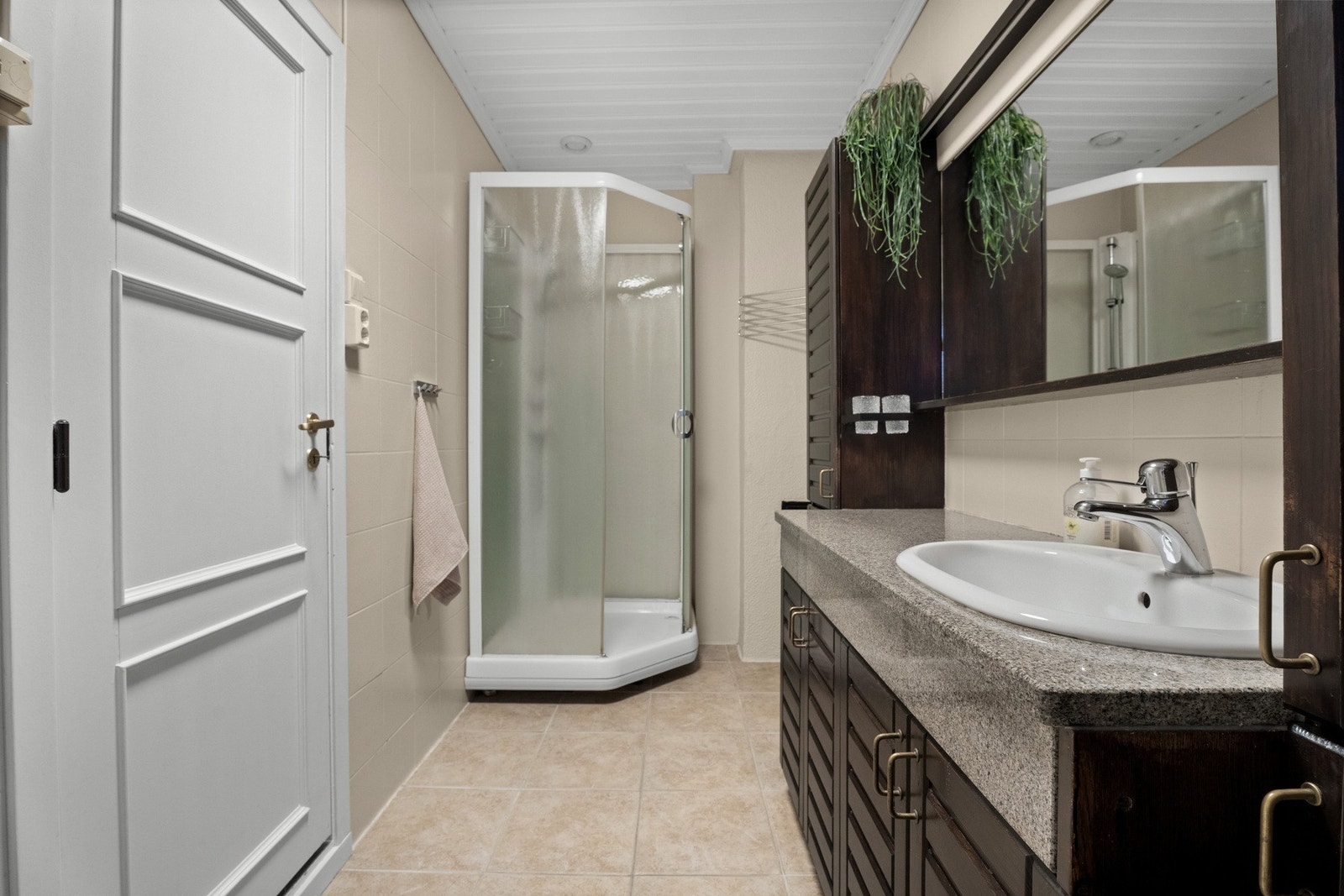 Flislagt bad innredet med dusjkabinett, gulvstående toalett og benkeskap med servant. Galleribilde