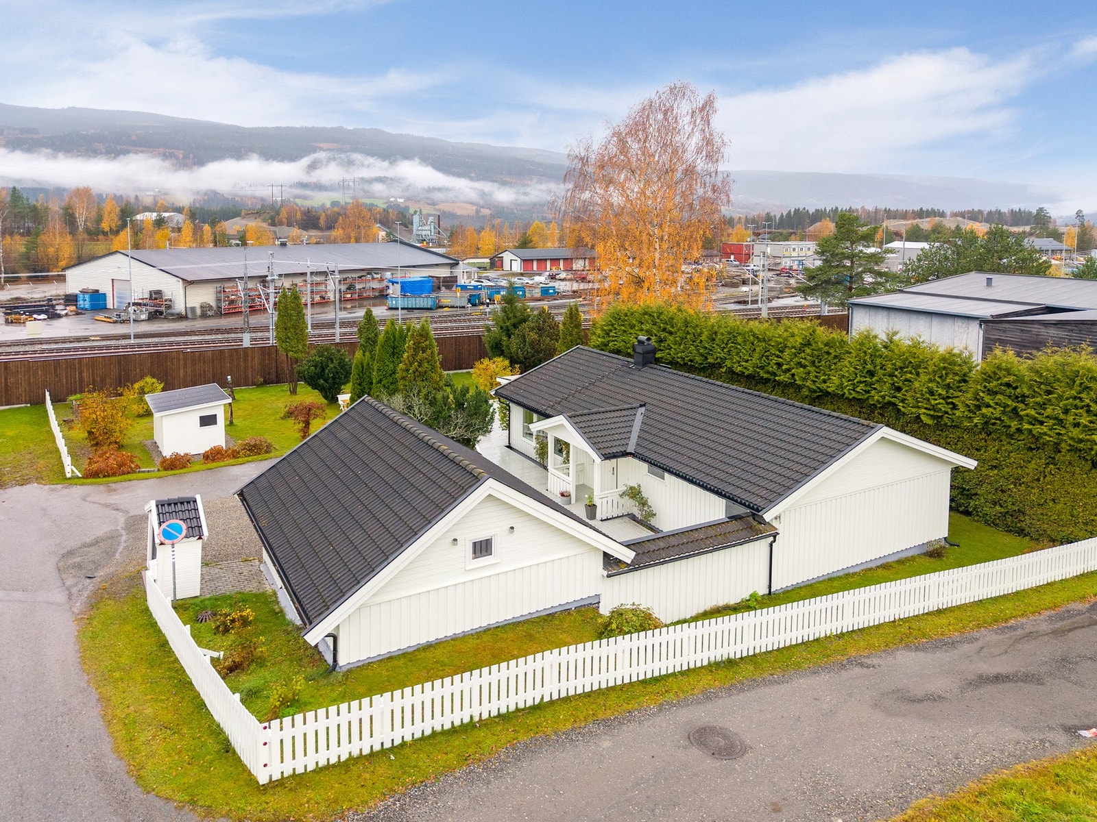 Pent opparbeidet tomt med innkjørsel, garasje og hvitmalt gjerde som rammer inn eiendommen på klassisk vis. Galleribilde