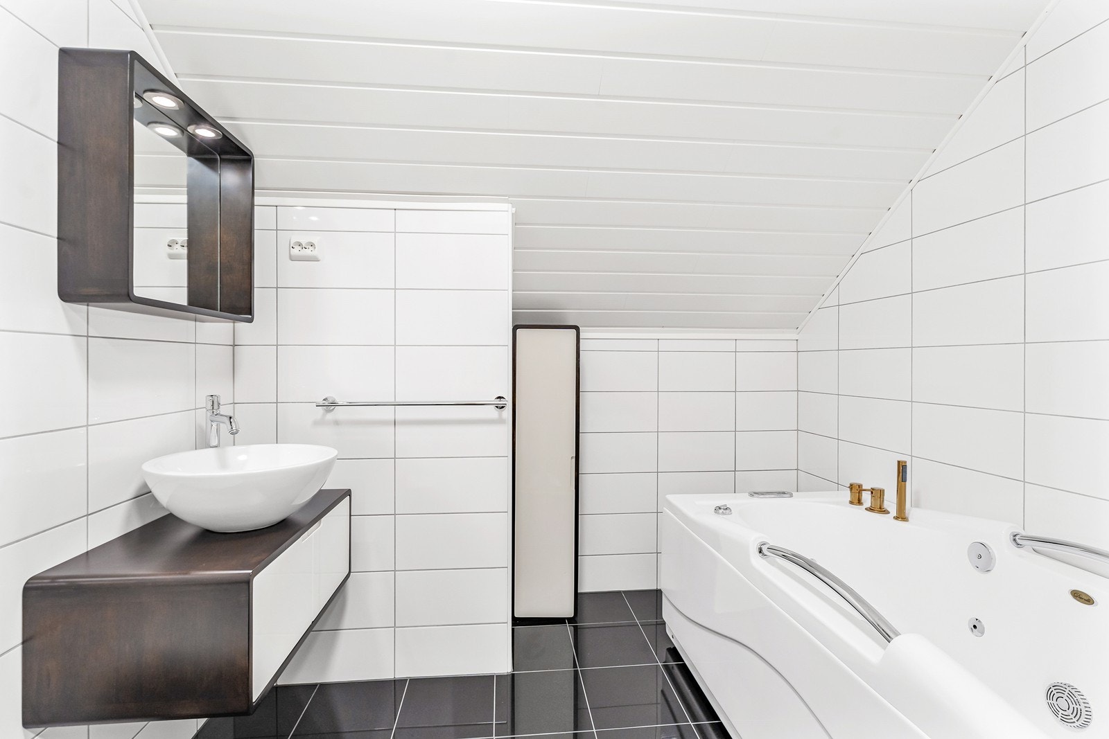 Badet er innredet med servant med skapinnredning, vegghengt toalett og badekar Galleribilde