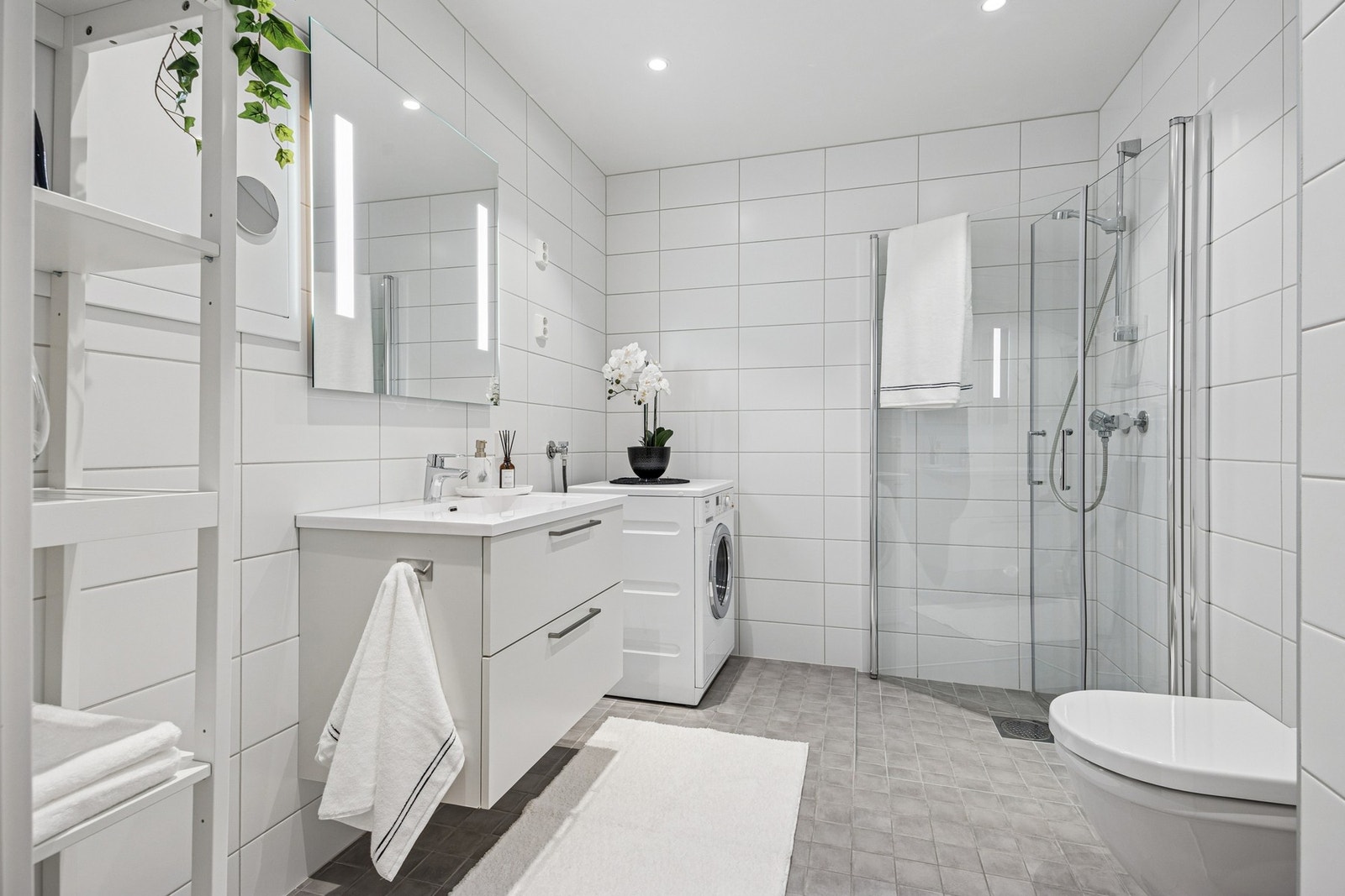 Delikat baderom fra byggeår på ca. 6 kvm, med fliser på både gulv og vegger samt behagelig gulvvarme. Rommet har moderne innredning med dusjhjørne med glassdører, vegghengt toalett og opplegg for vaskemaskin. Galleribilde