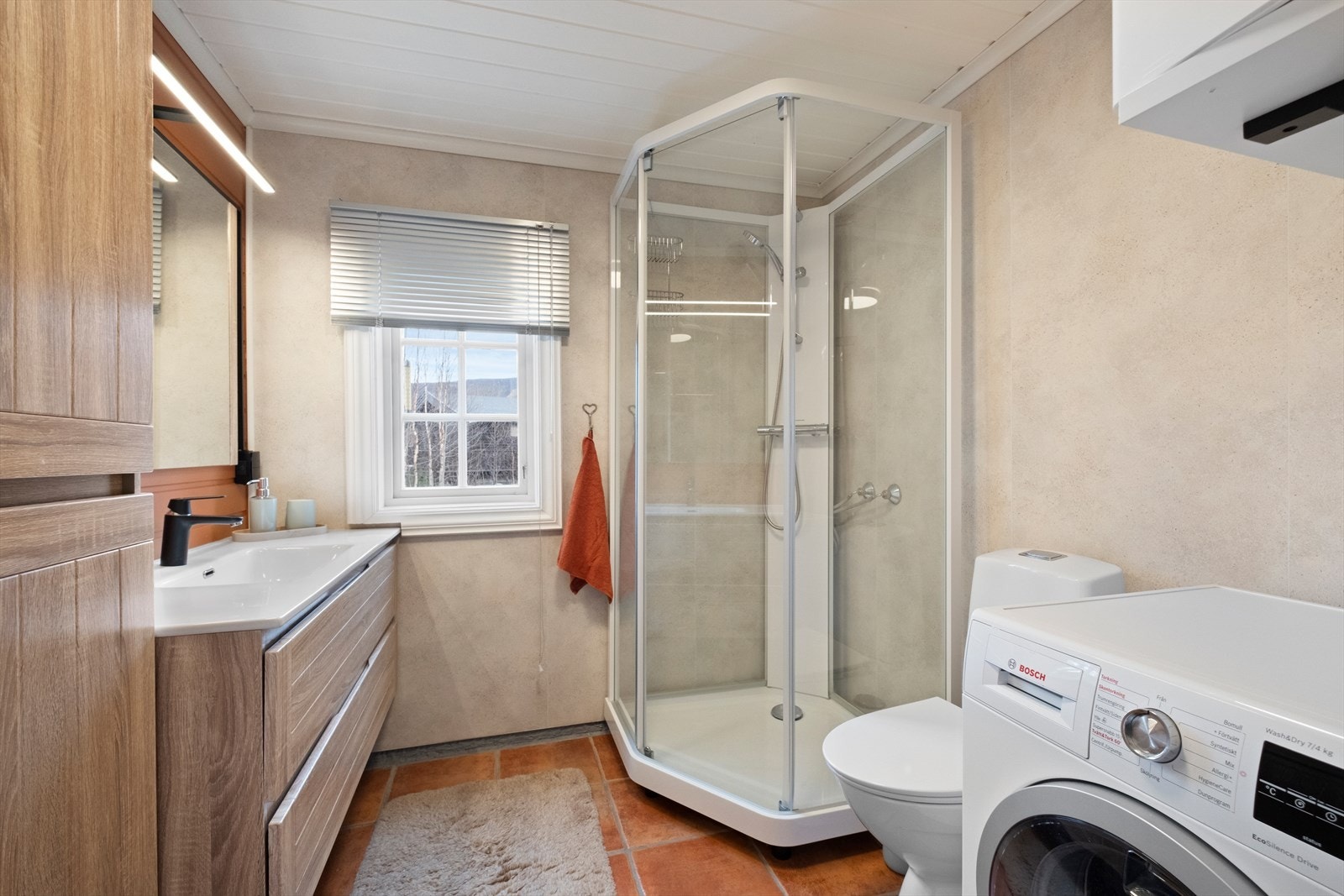 Badet er utstyrt med dusjkabinett, toalett, innredning med servant og opplegg for vaskemaskin. Galleribilde