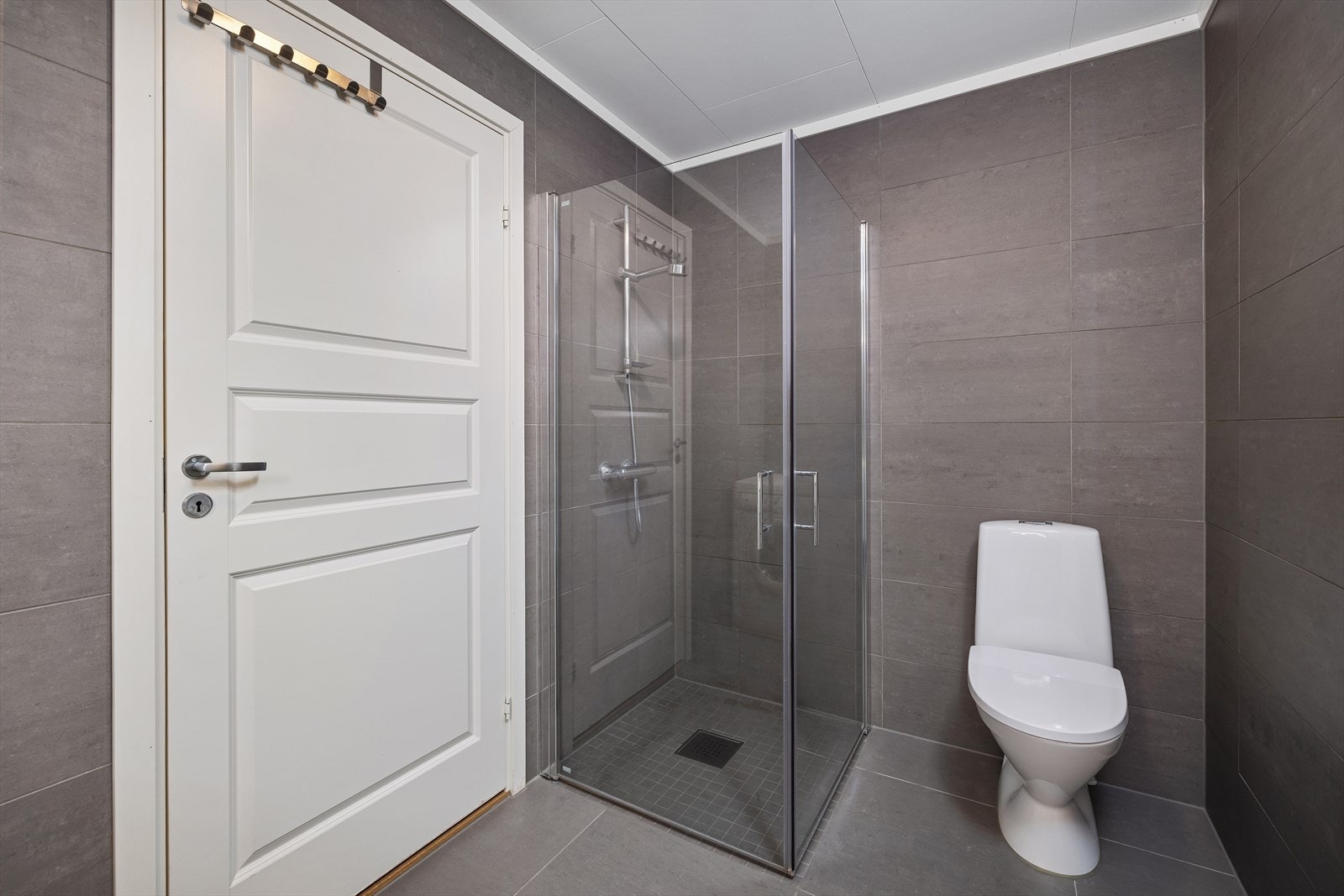 Badet har innredning med veggmontert toalett, dusjvegger/hjørne. Det er varmekabler på gulvet. Galleribilde