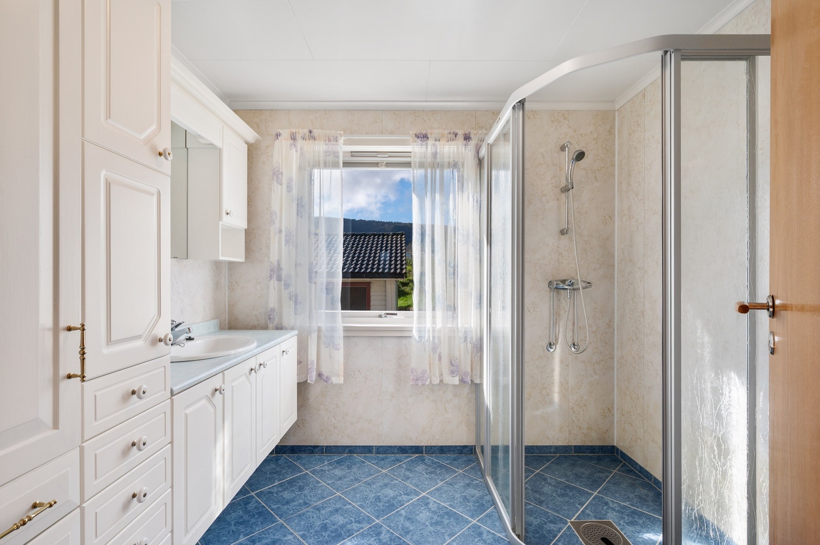 Eldre bad med flislagt gulv og baderomsplater på vegger. Det er varmekabler i gulvet. Galleribilde