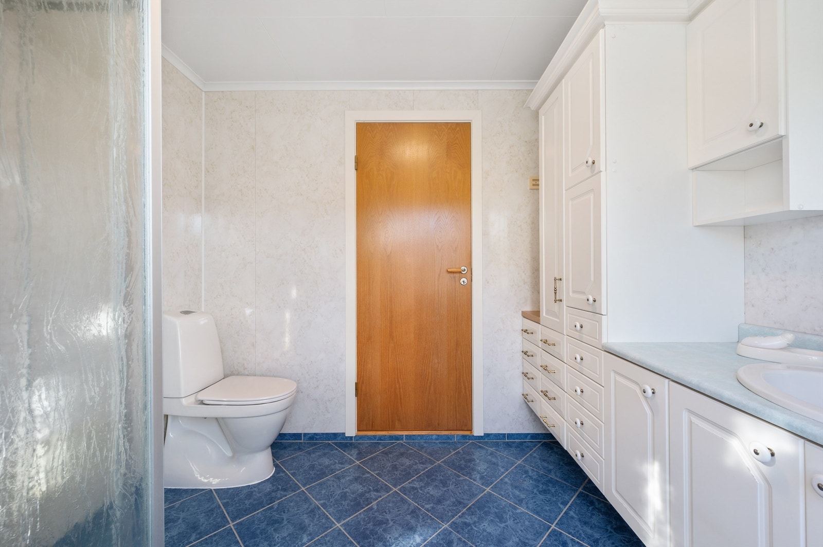 Innredet med vegghengt servantløsning, speil med overlys, dusjvegger og gulvstående toalett. Galleribilde