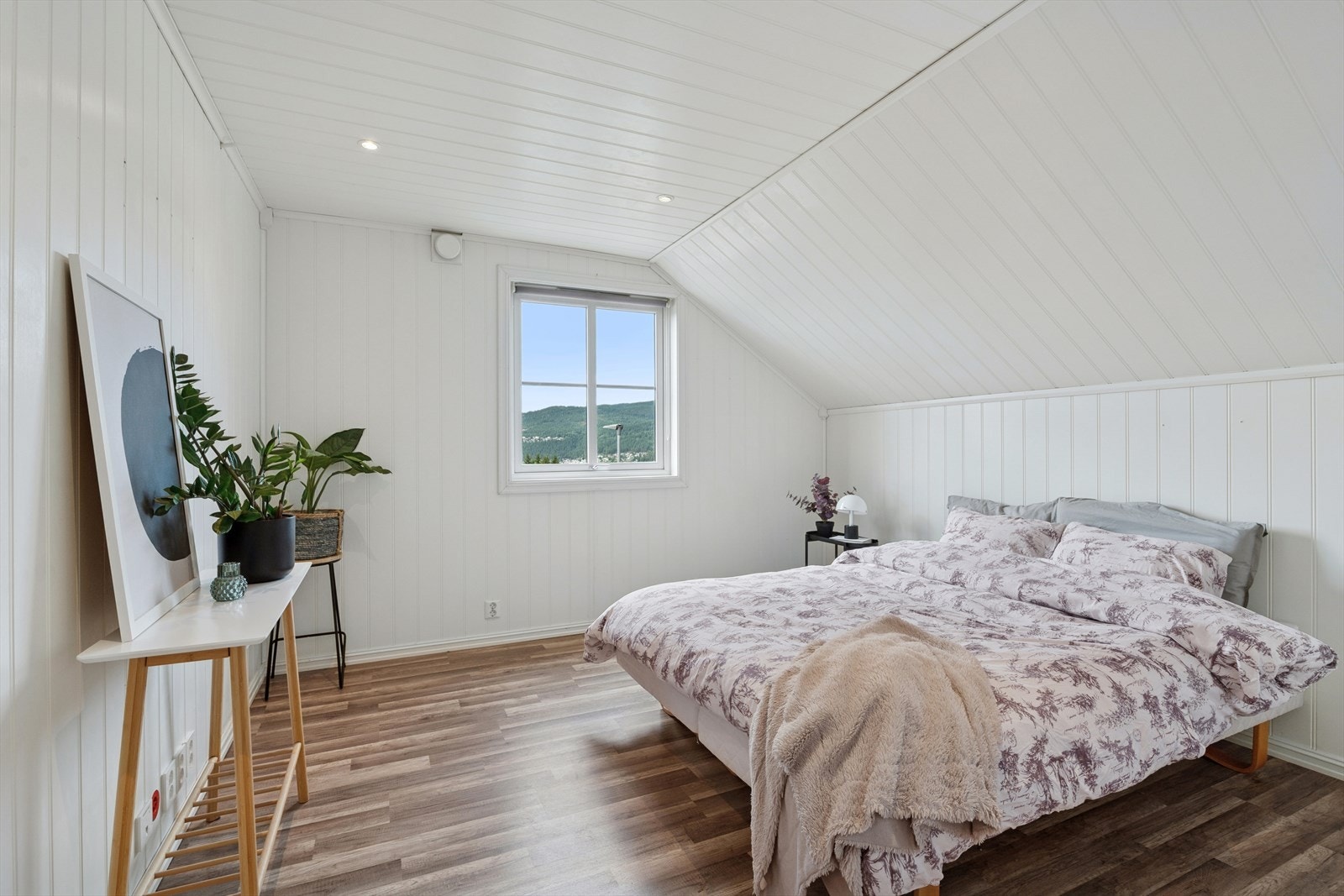 Lyst og stilrent soverom med plass til dobbeltseng og skråtak med downlights gir en lun og moderne atmosfære. Galleribilde