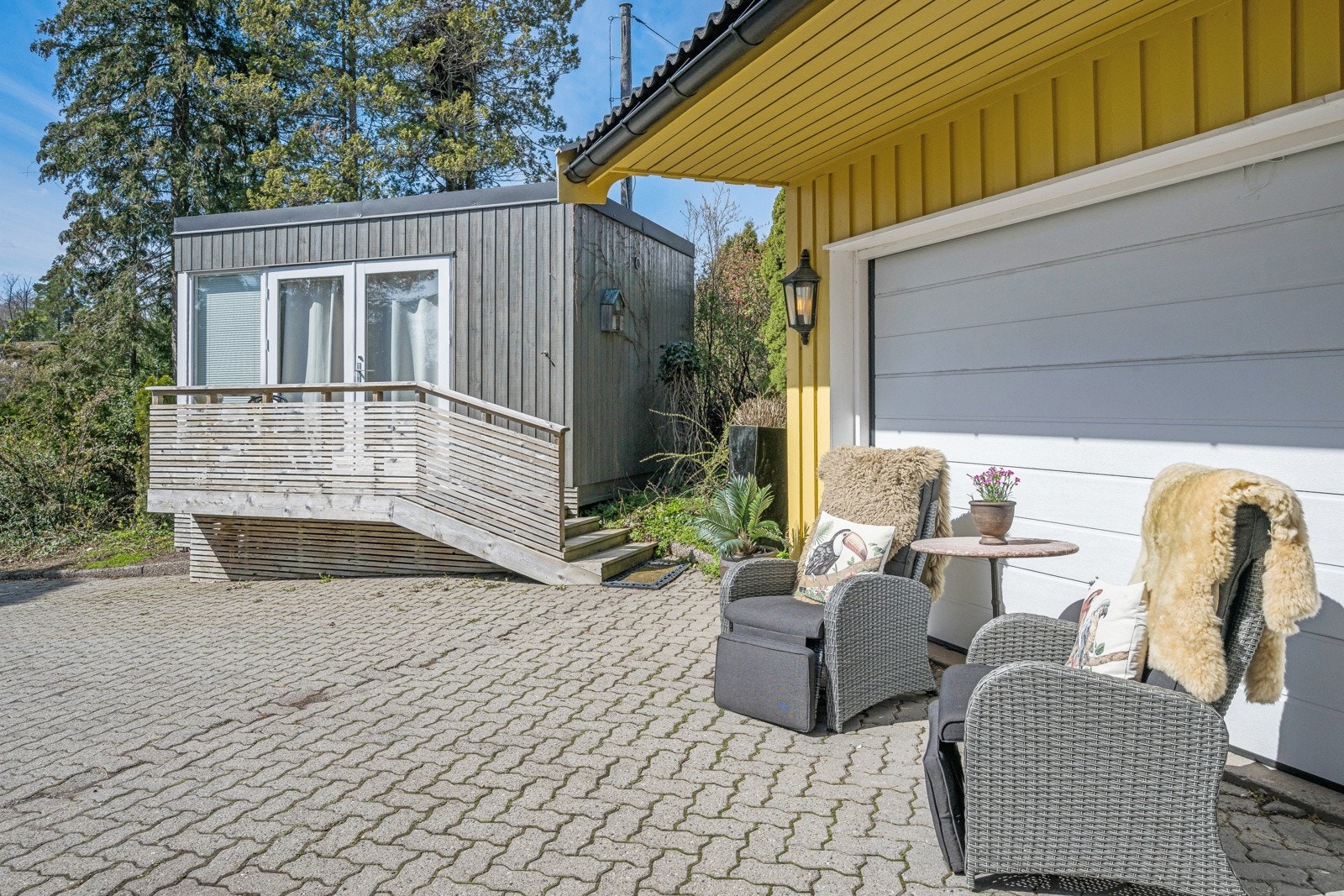 Da er vi på fremsiden av huset hvor vi finner en solrik krok ved garasjen - vi ser også annekset til venstre i bildet Galleribilde