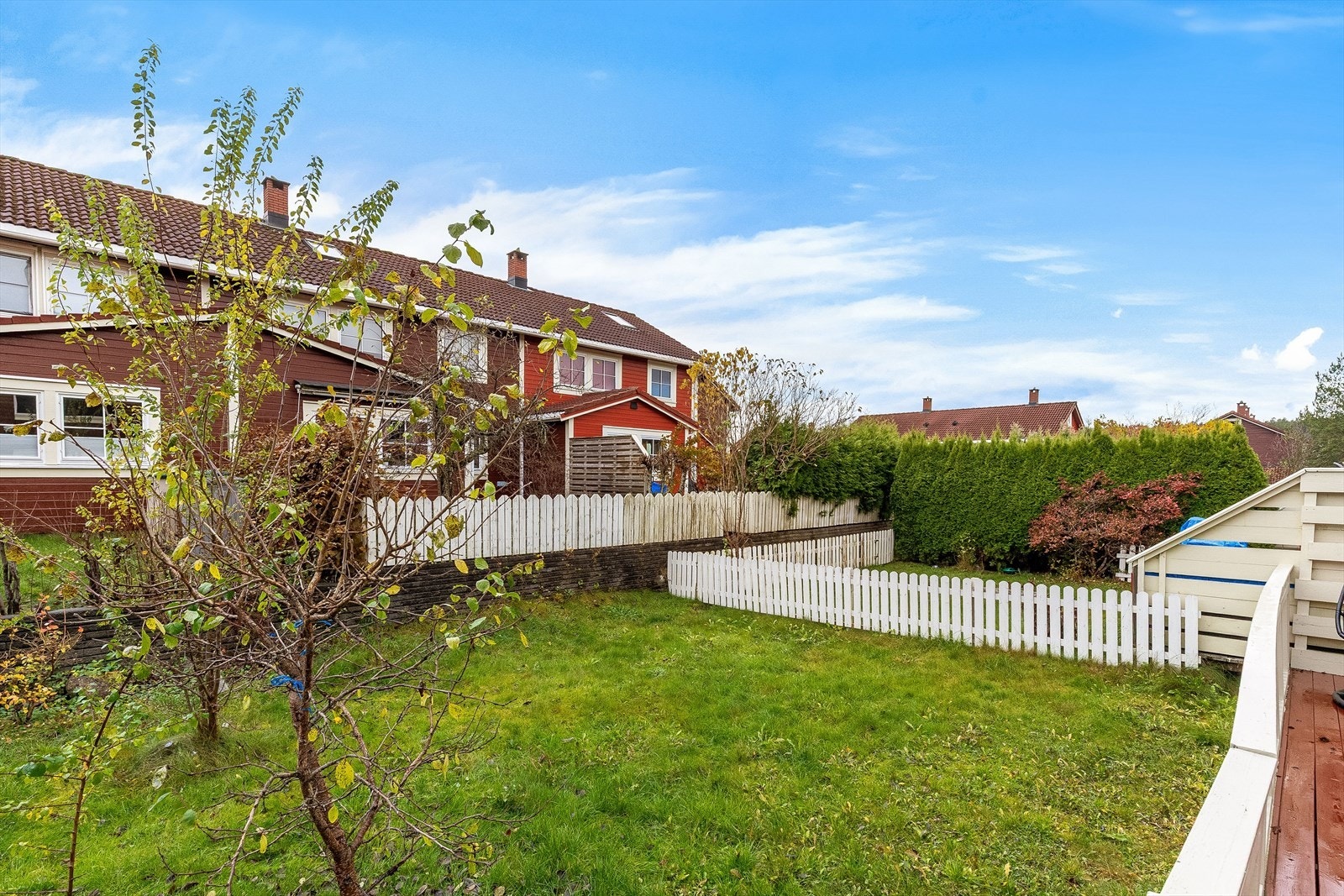 Utenfor terrassen er det en inngjerdet hage som er pent beplantet med plen, prydbusker, bed og trær. Galleribilde