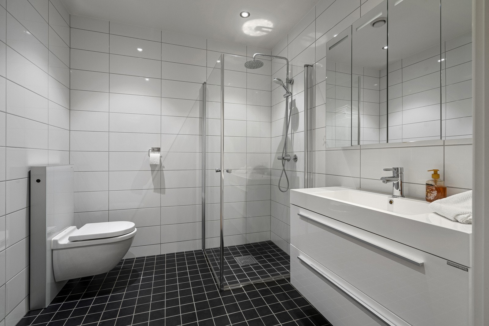 Pent og flislagt bad med dusjhjørne, wc og servant med over/underskap. Galleribilde